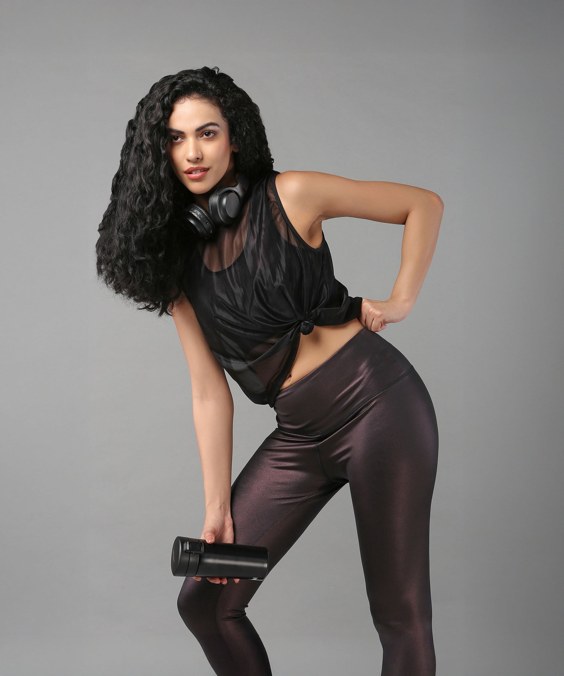 Stylish black sheer top for women paired with shiny leggings and headphones for an active look