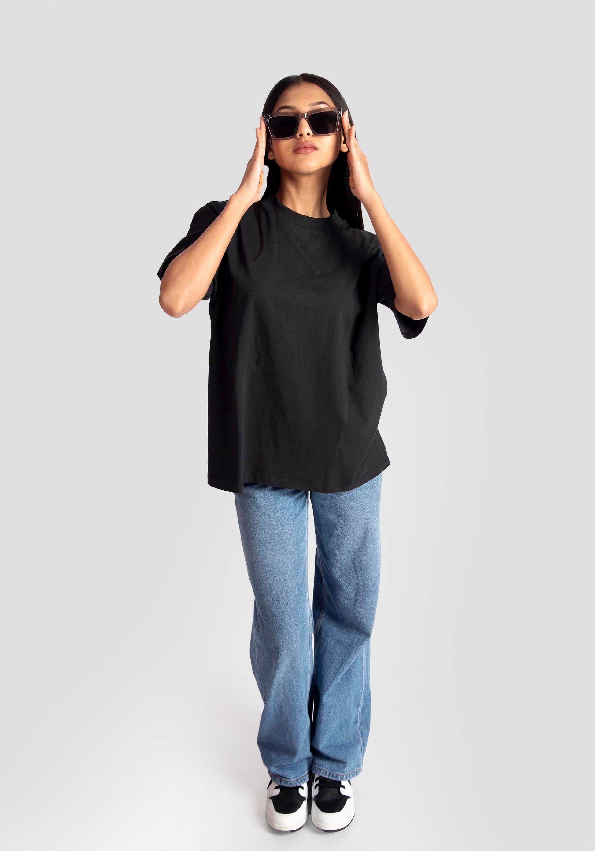 Woman wearing black streetwear oversized tee womens with blue jeans and sunglasses by Stylera
