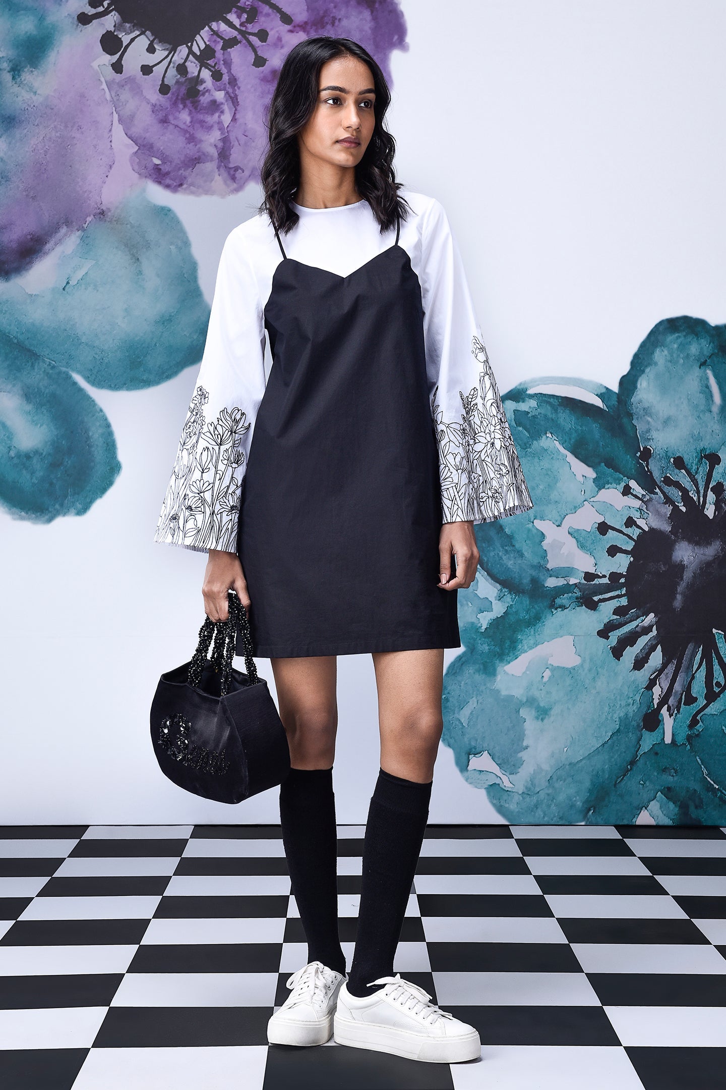 Stylera model wearing black white layered dress over printed bell sleeve tee with knee socks and sneakers