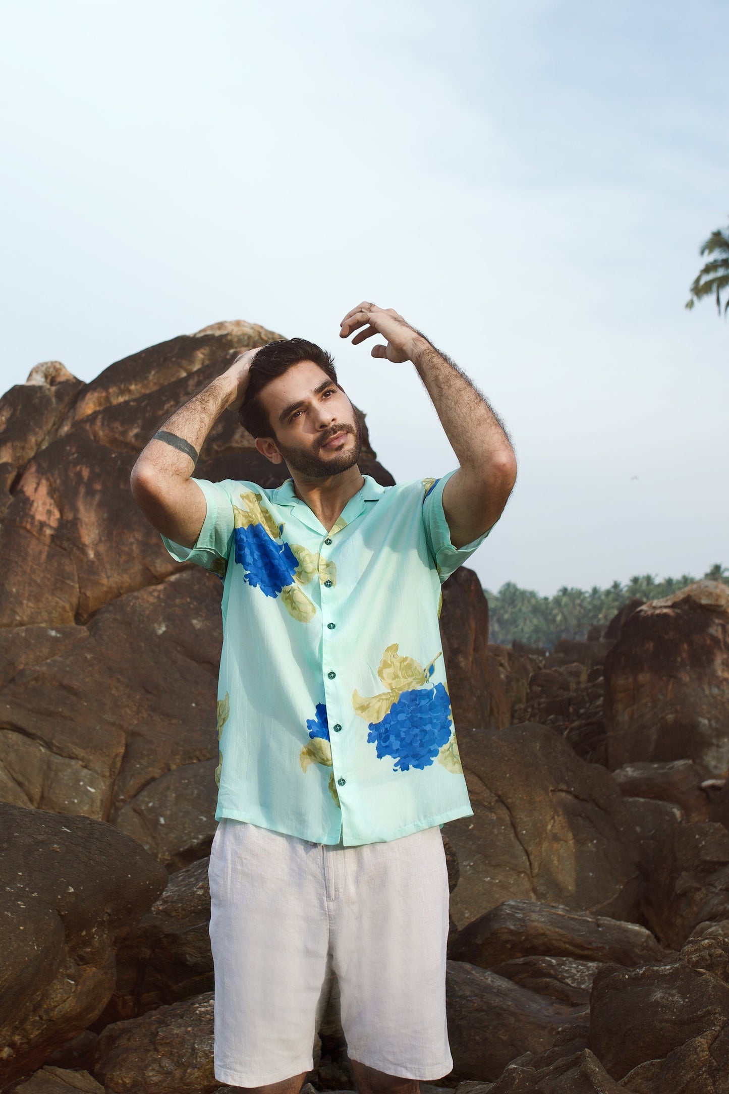 Man wearing a Stylera blue oversized shirt for men with colorful floral prints while posing outdoors