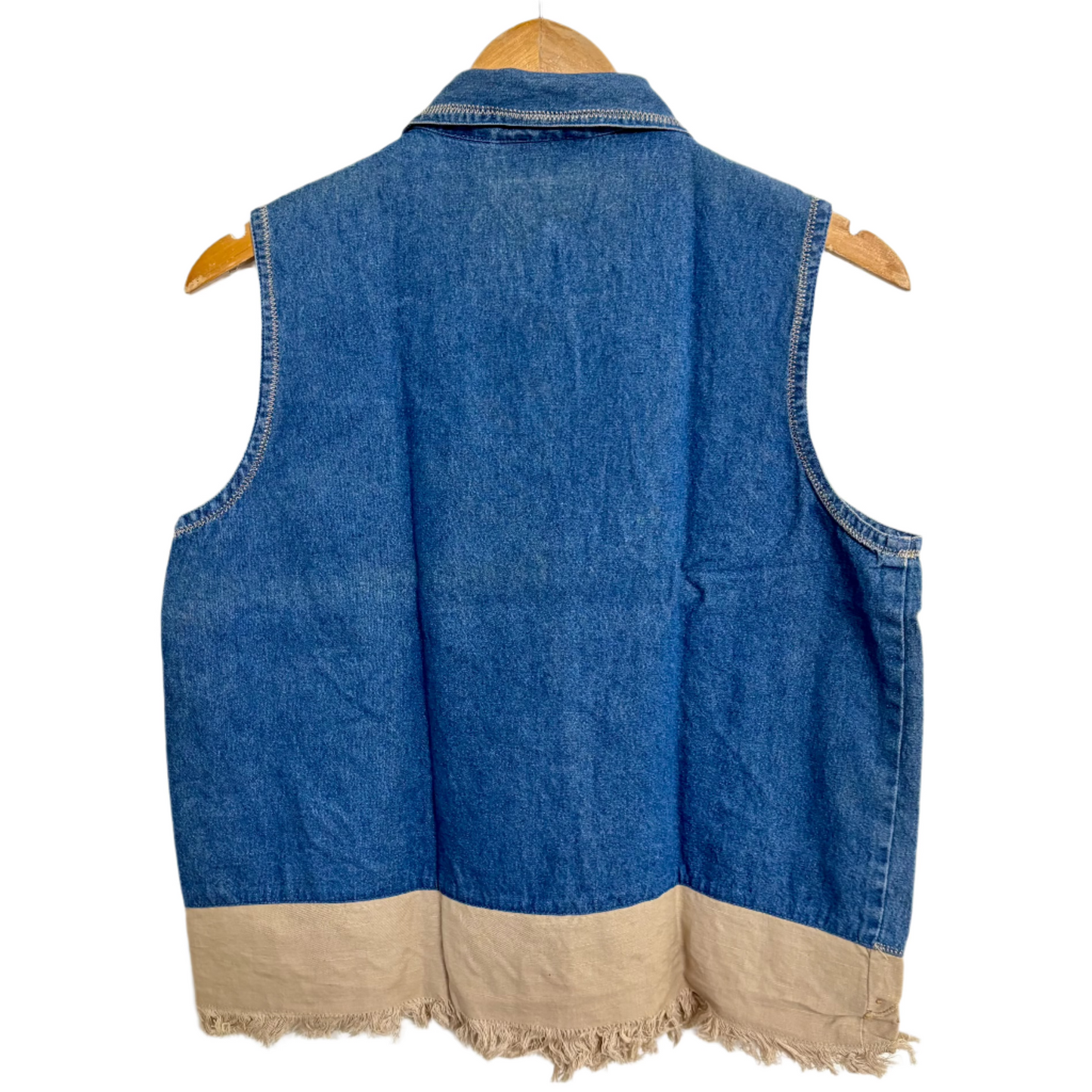 Embroidered denim vest for women back view showing plain blue back and tan frayed hem on wooden hanger