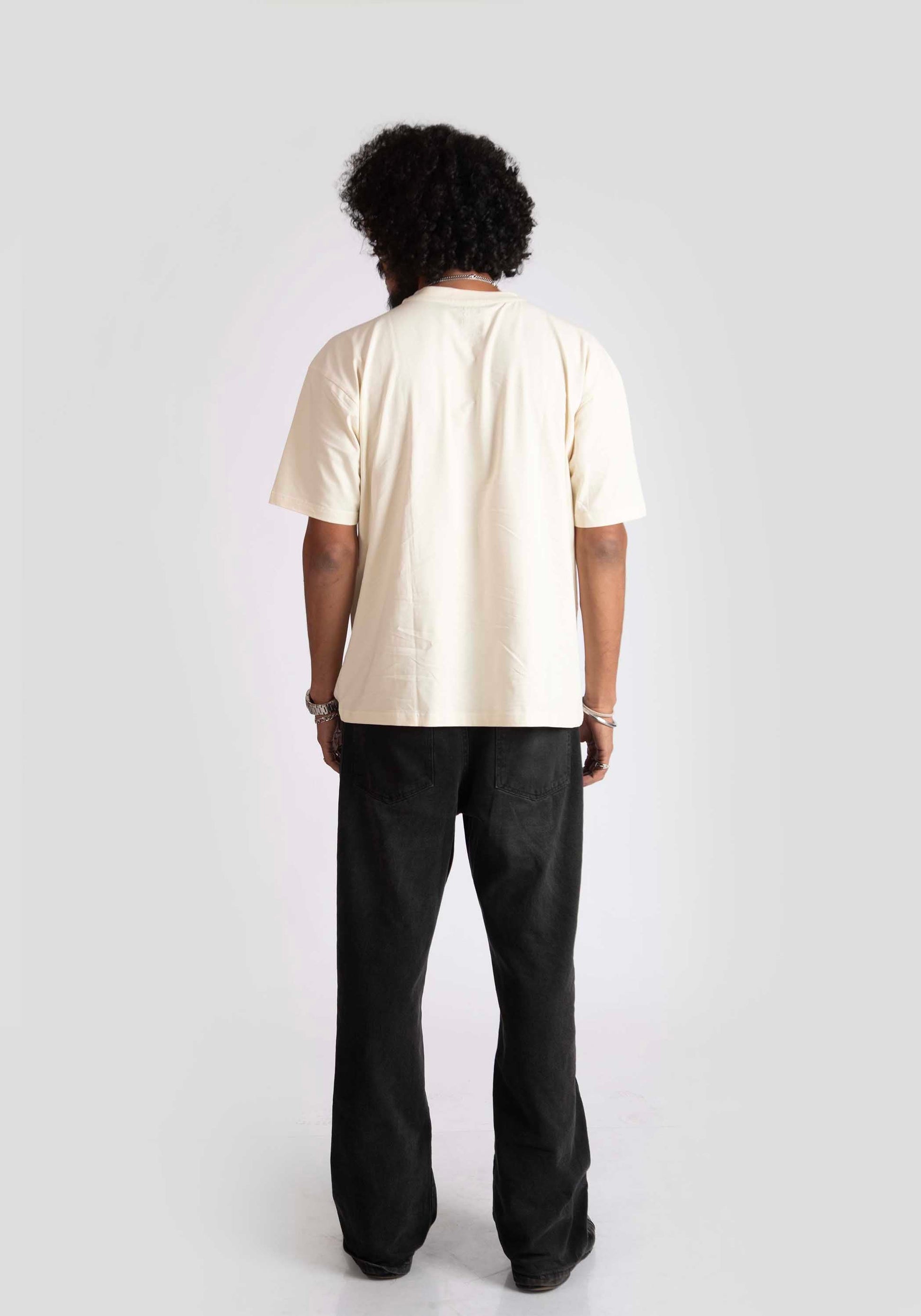 Back view of male model wearing Stylera cyberpunk oversized t-shirt in cream with black pants