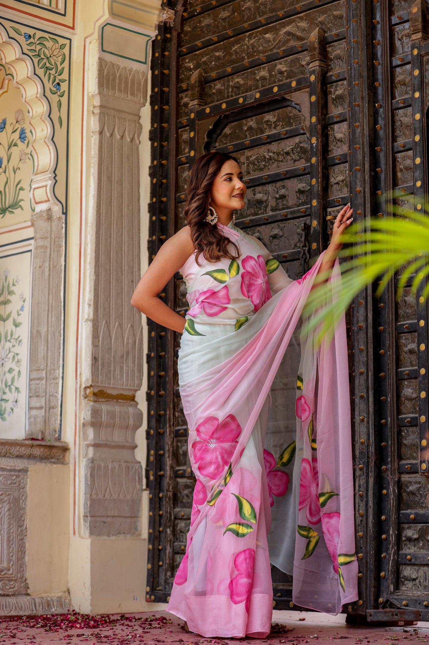 Elegant woman in a pink floral chiffon saree posing by a traditional door, perfect to buy trendy chiffon saree