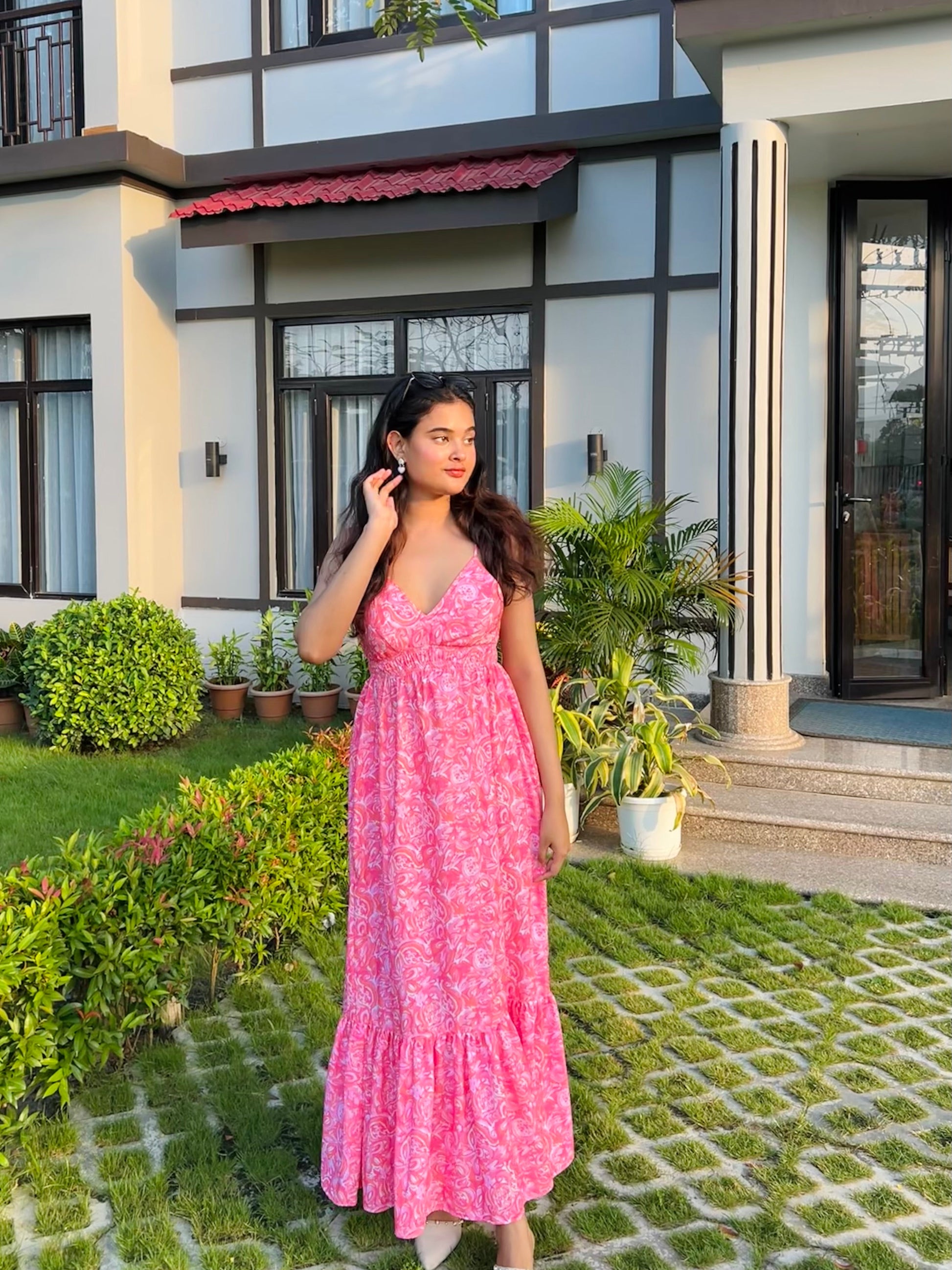 Woman in a pink casual floral maxi dress from Stylera standing on lawn by modern house