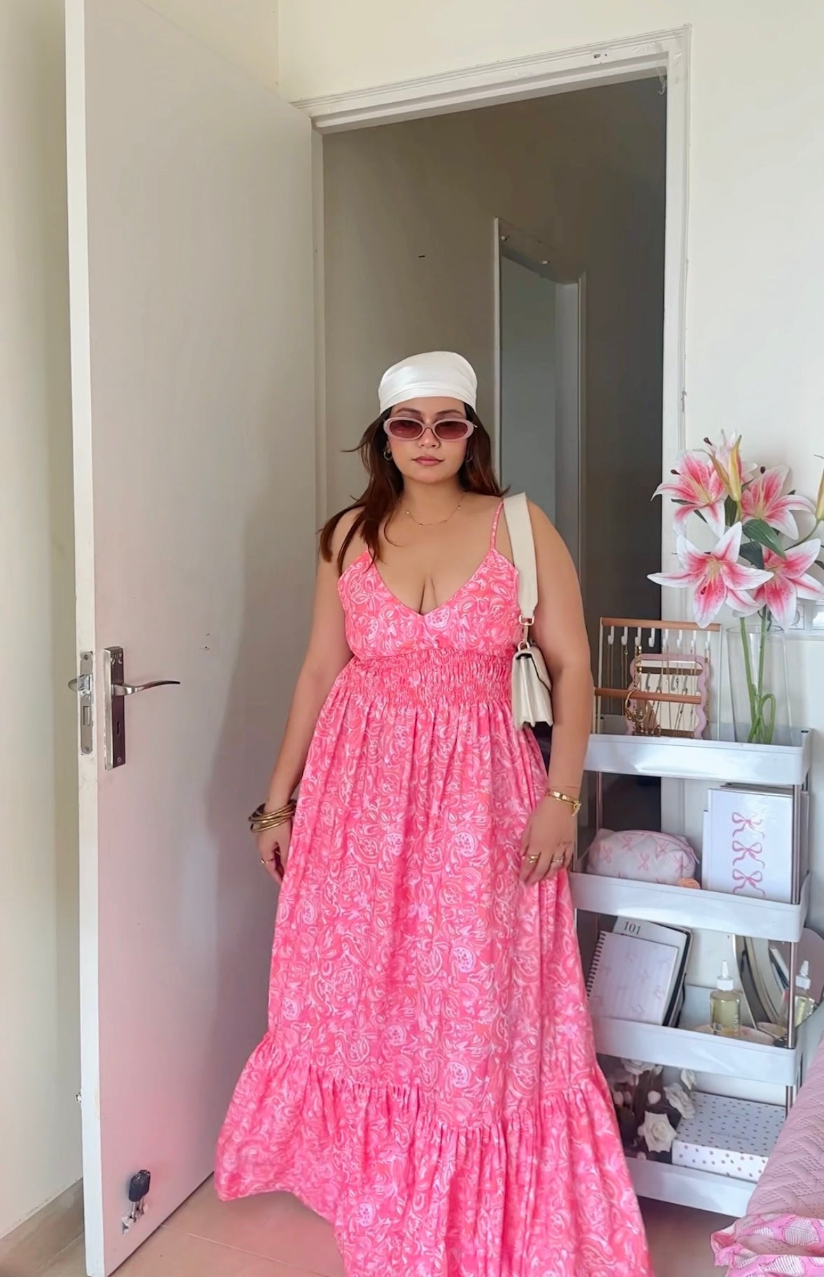 Woman in Stylera casual floral maxi dress in pink with ruffle hem white cap sunglasses and shoulder bag