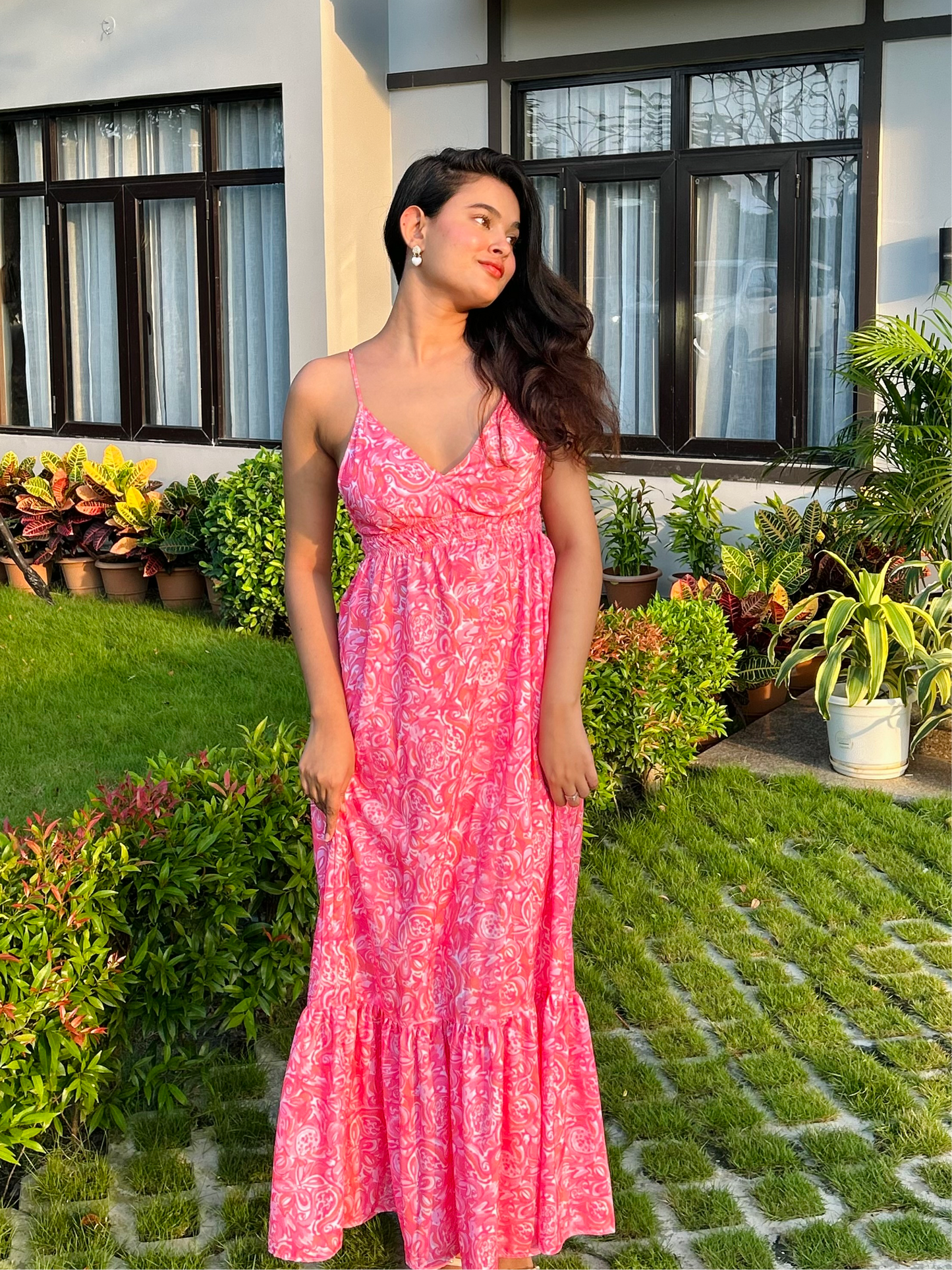 Woman in pink printed casual floral maxi dress with spaghetti straps and ruffled hem standing in garden