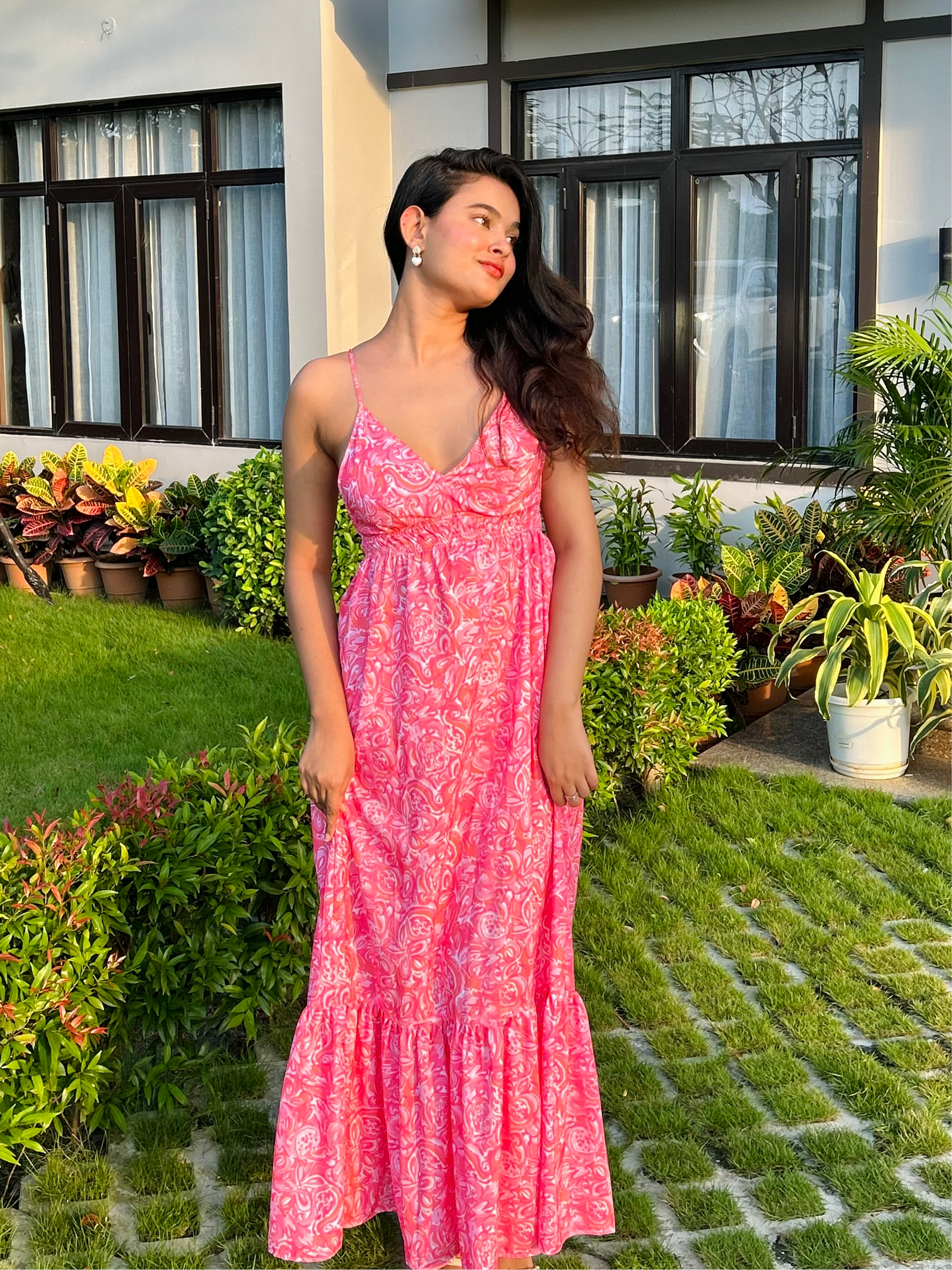 Woman in pink printed casual floral maxi dress with spaghetti straps and ruffled hem standing in garden