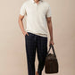Casual linen polo for men in cream with a relaxed fit, paired with checked pants and a stylish bag.
