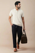 Casual linen polo for men in cream with a relaxed fit, paired with checked pants and a stylish bag.