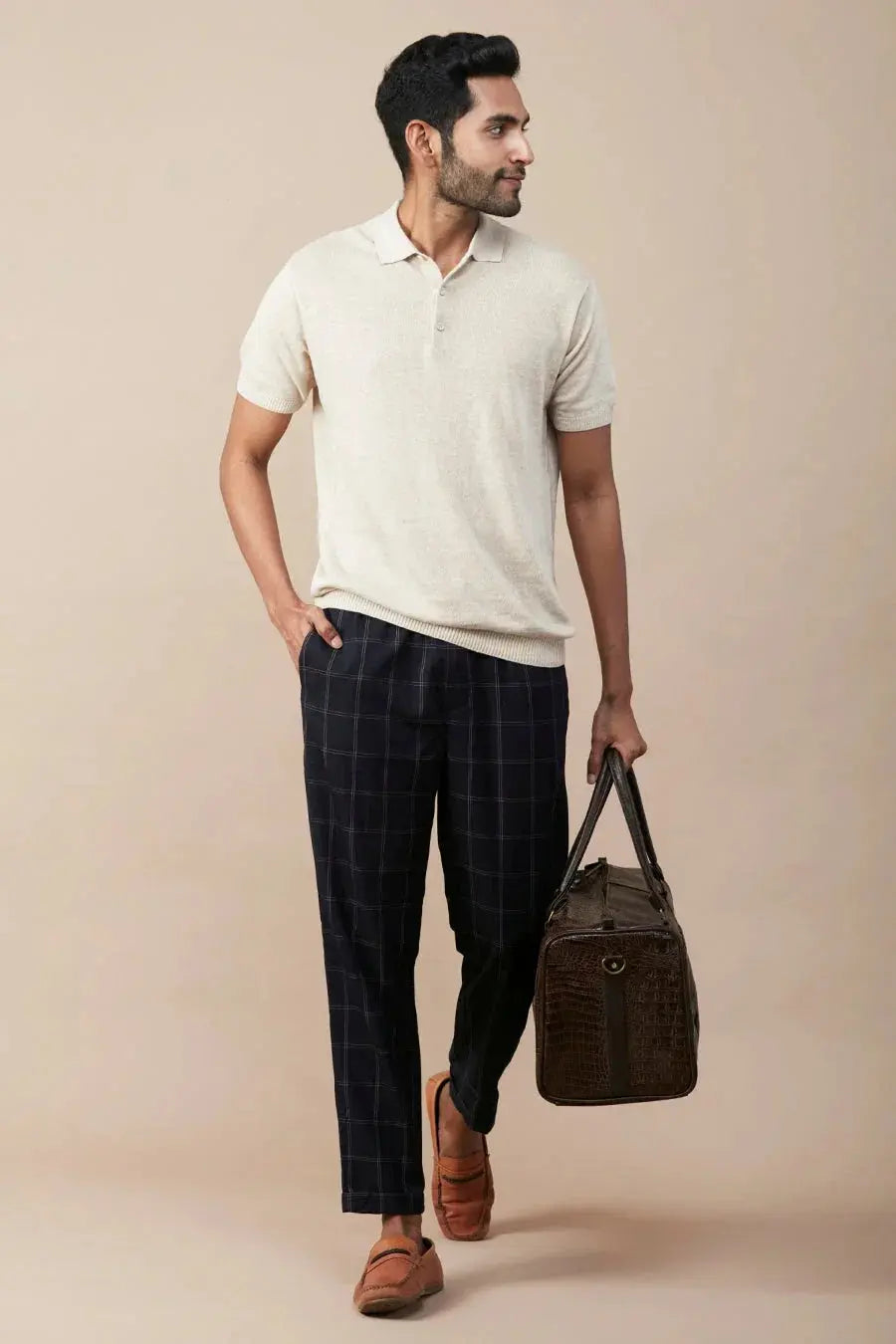 Casual linen polo for men in cream with a relaxed fit, paired with checked pants and a stylish bag.