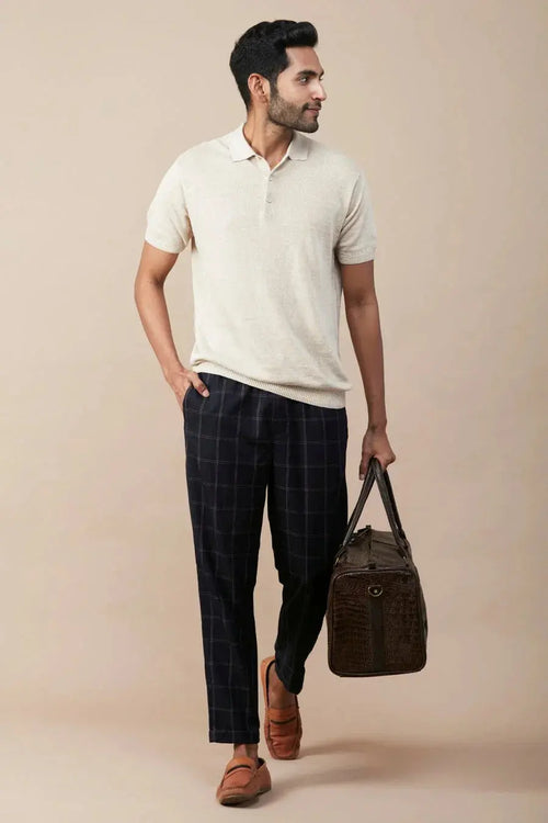 Casual linen polo for men in cream with a relaxed fit, paired with checked pants and a stylish bag.