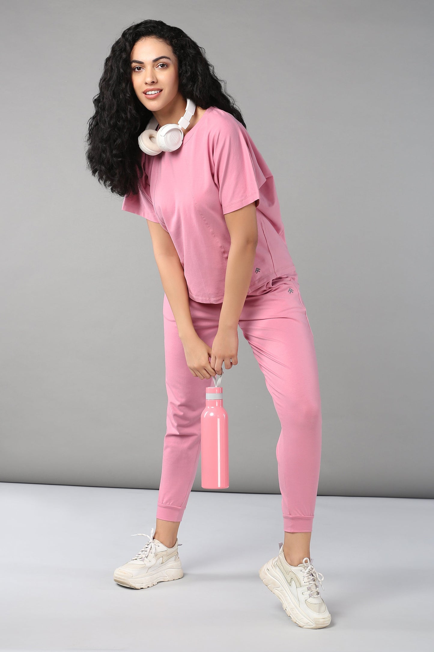 Woman in casual pink lounge wear for women, holding a pink water bottle and wearing headphones