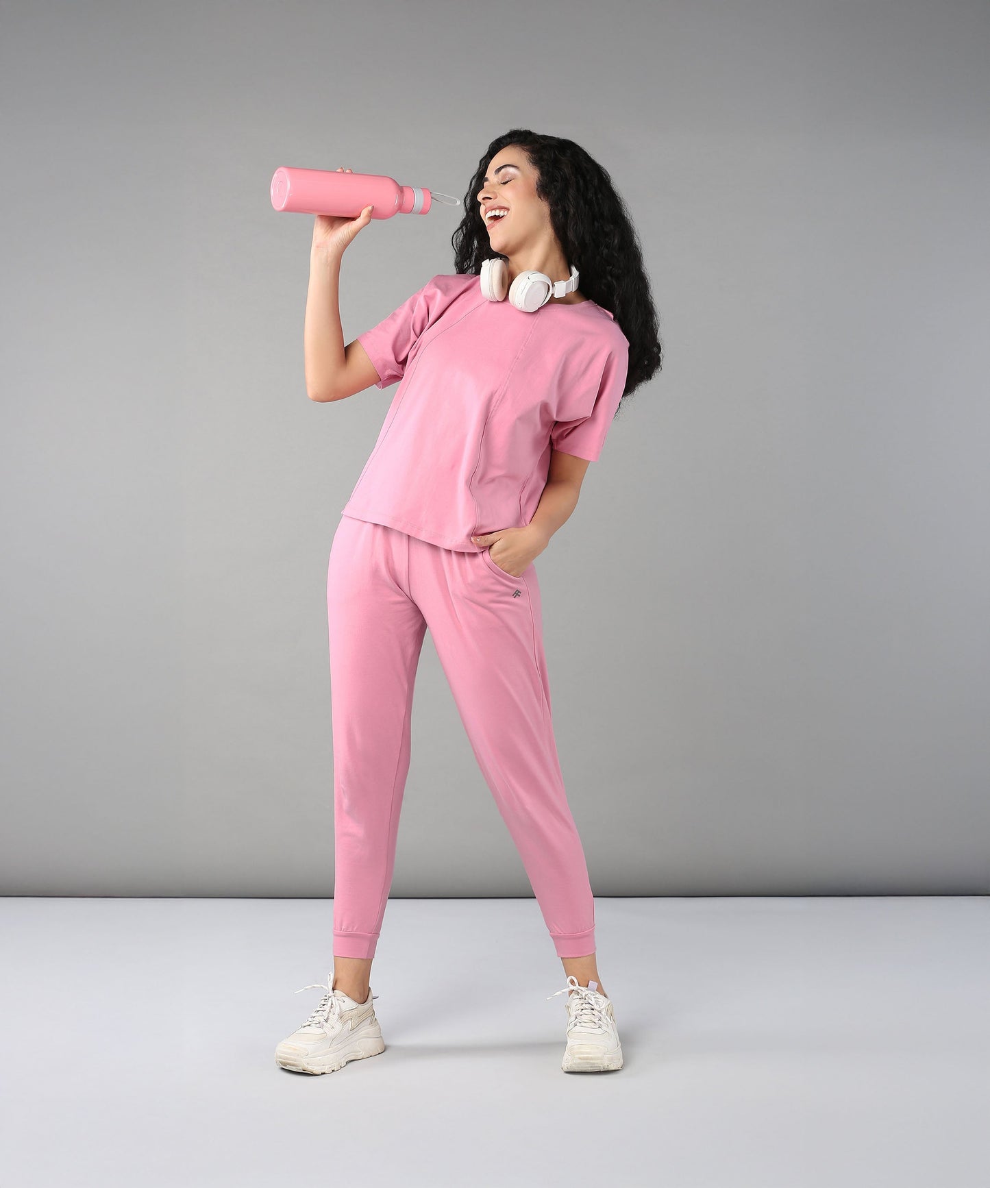 Woman wearing casual pink lounge wear for women, holding a pink water bottle with headphones on.