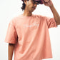 Model wearing Stylera casual pink slogan tee for women oversized fit with white script logo and jeans