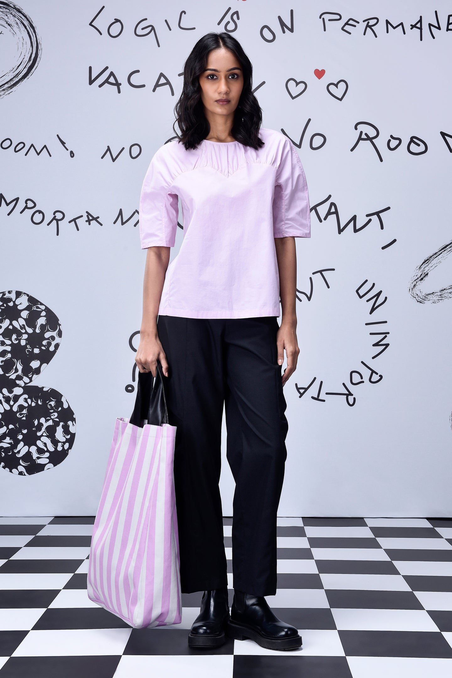 Stylera casual pink top for women worn with black trousers and striped tote on checkered floor