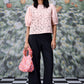 Stylera model wearing a pink lace casual semi fit top for women with puff sleeves and black trousers