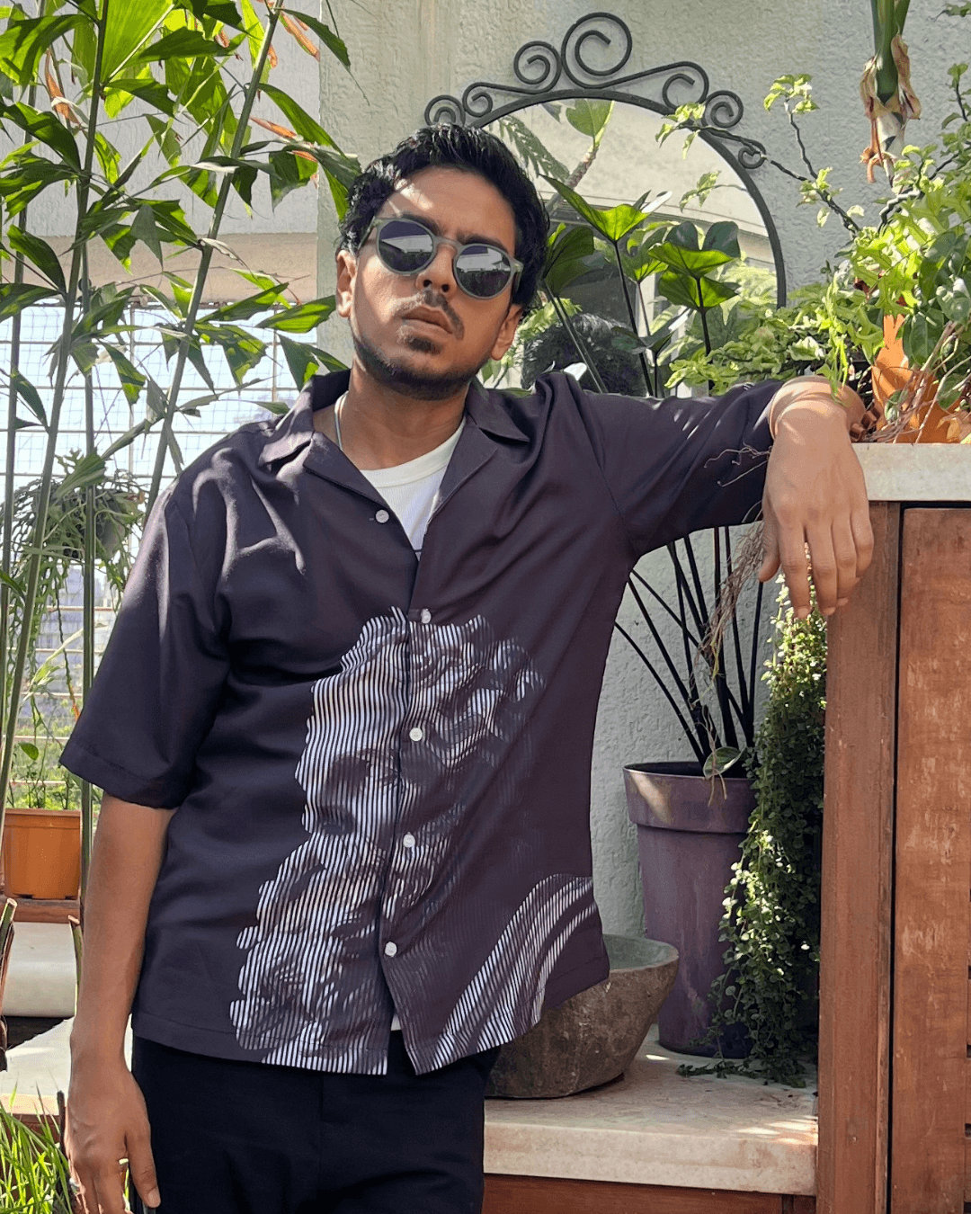 Stylera black short sleeve printed shirt worn by man leaning on terrace with plants casual statement shirts for men