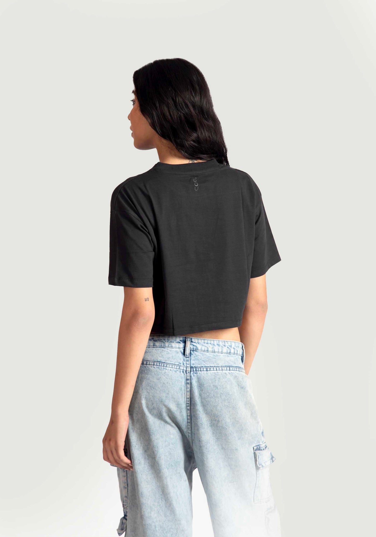 Back view of woman wearing charcoal black oversized crop top paired with light blue denim jeans