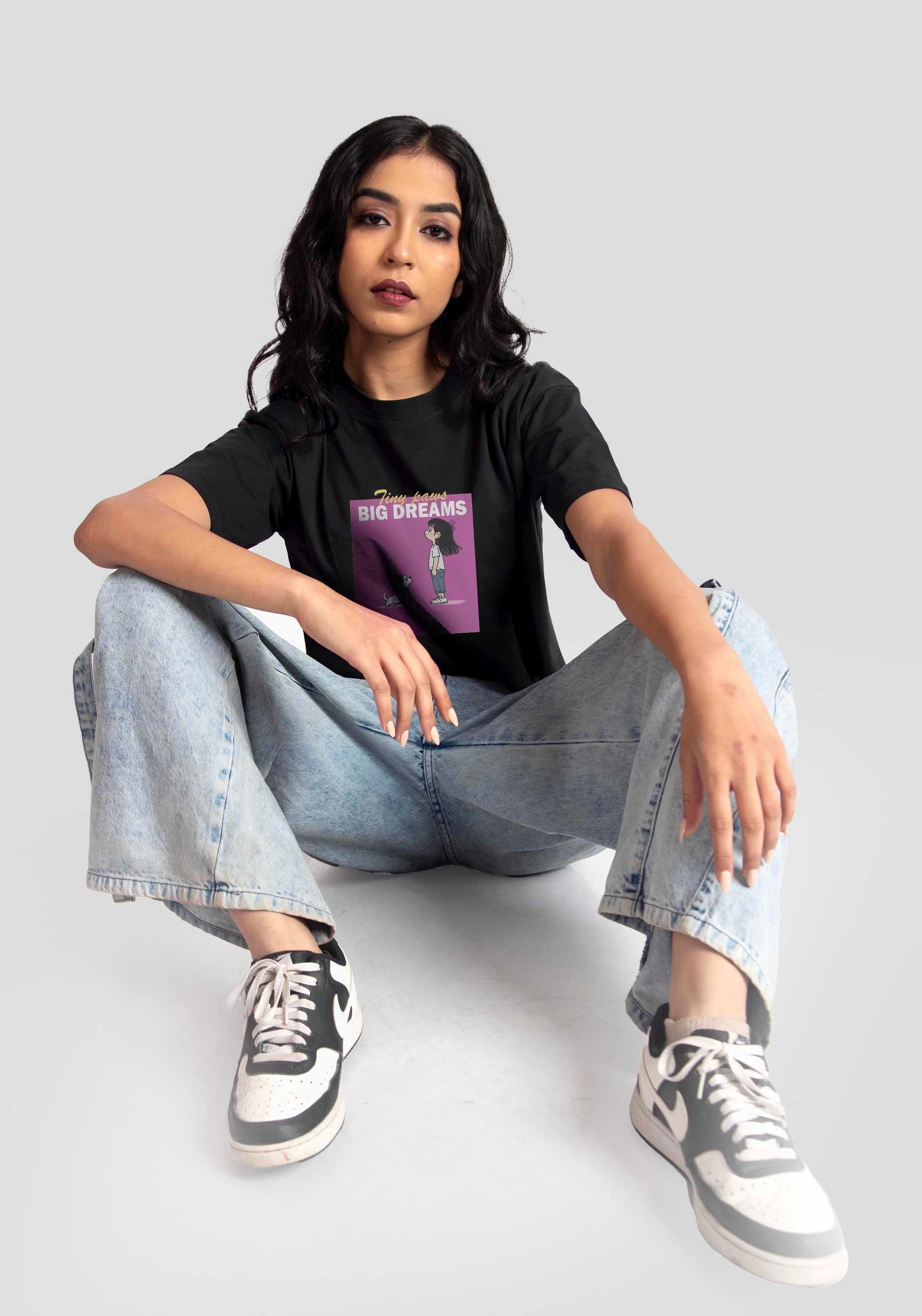 Woman wearing a charcoal black oversized crop top with graphic print paired with light blue jeans and sneakers