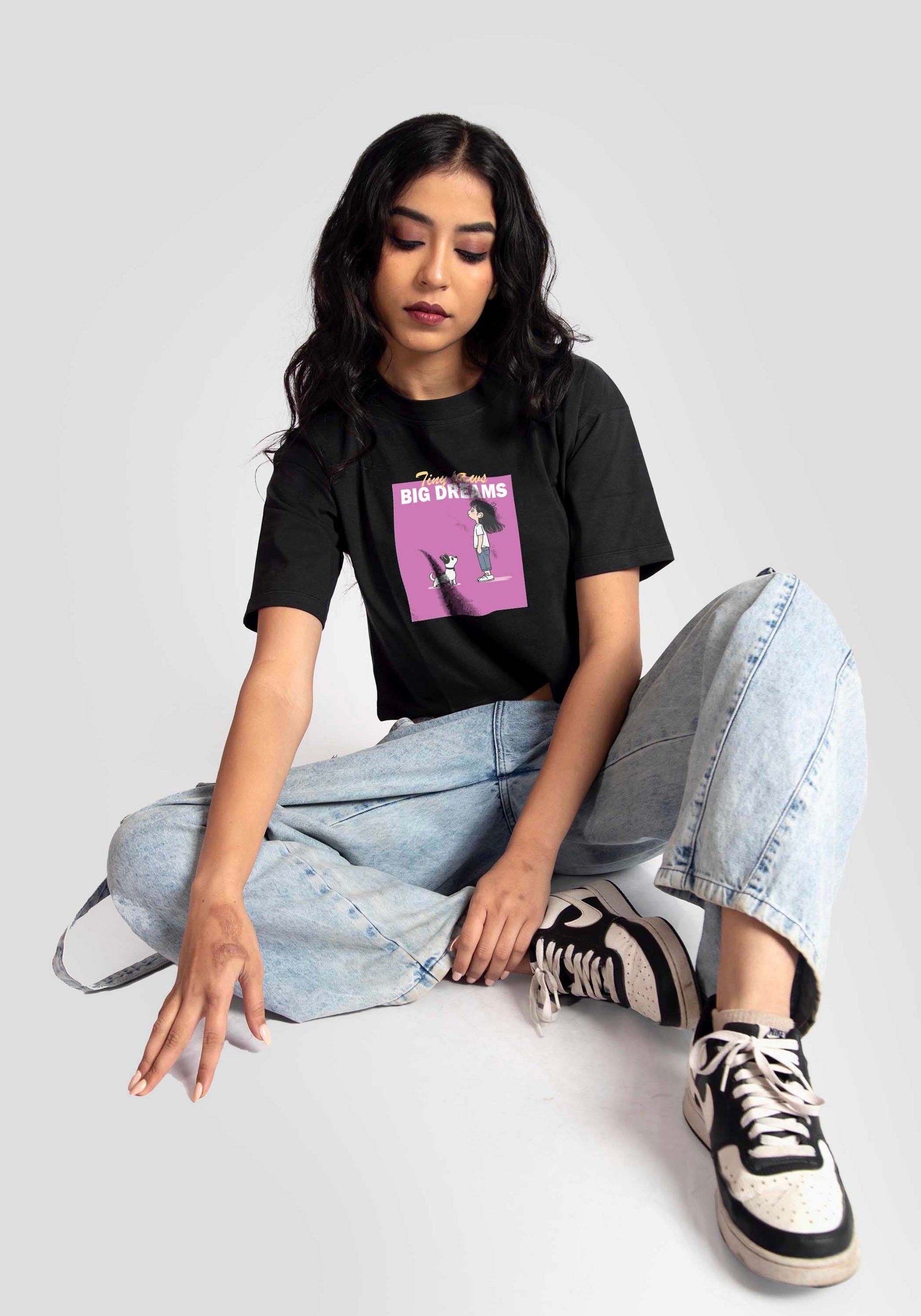 Stylera charcoal black oversized crop top worn by woman with graphic print paired with light blue jeans and sneakers