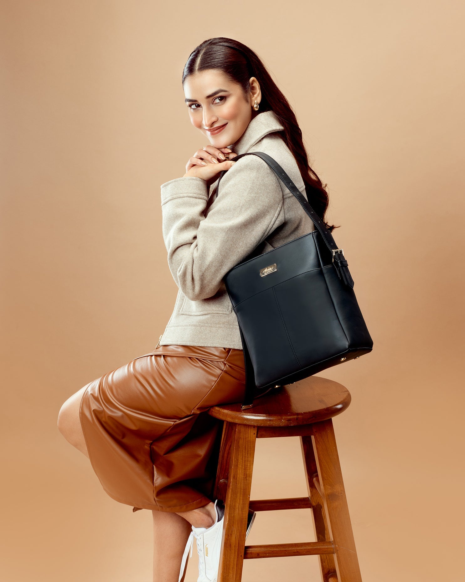 Fashion model showcasing charcoal chic bucket bag sitting on a stool in stylish attire