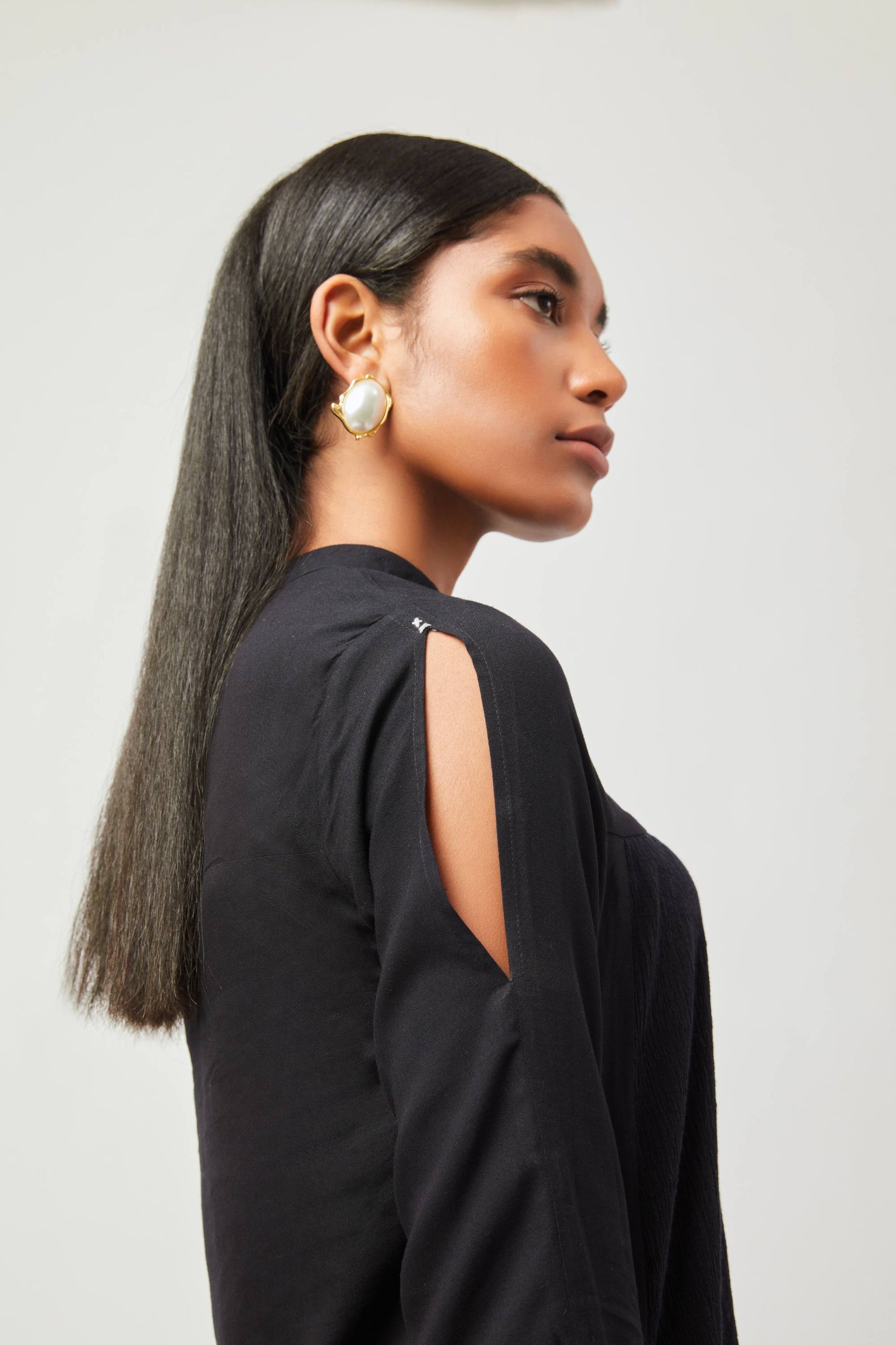 Stylera chic little black dress with open shoulder design worn by model with gold earrings