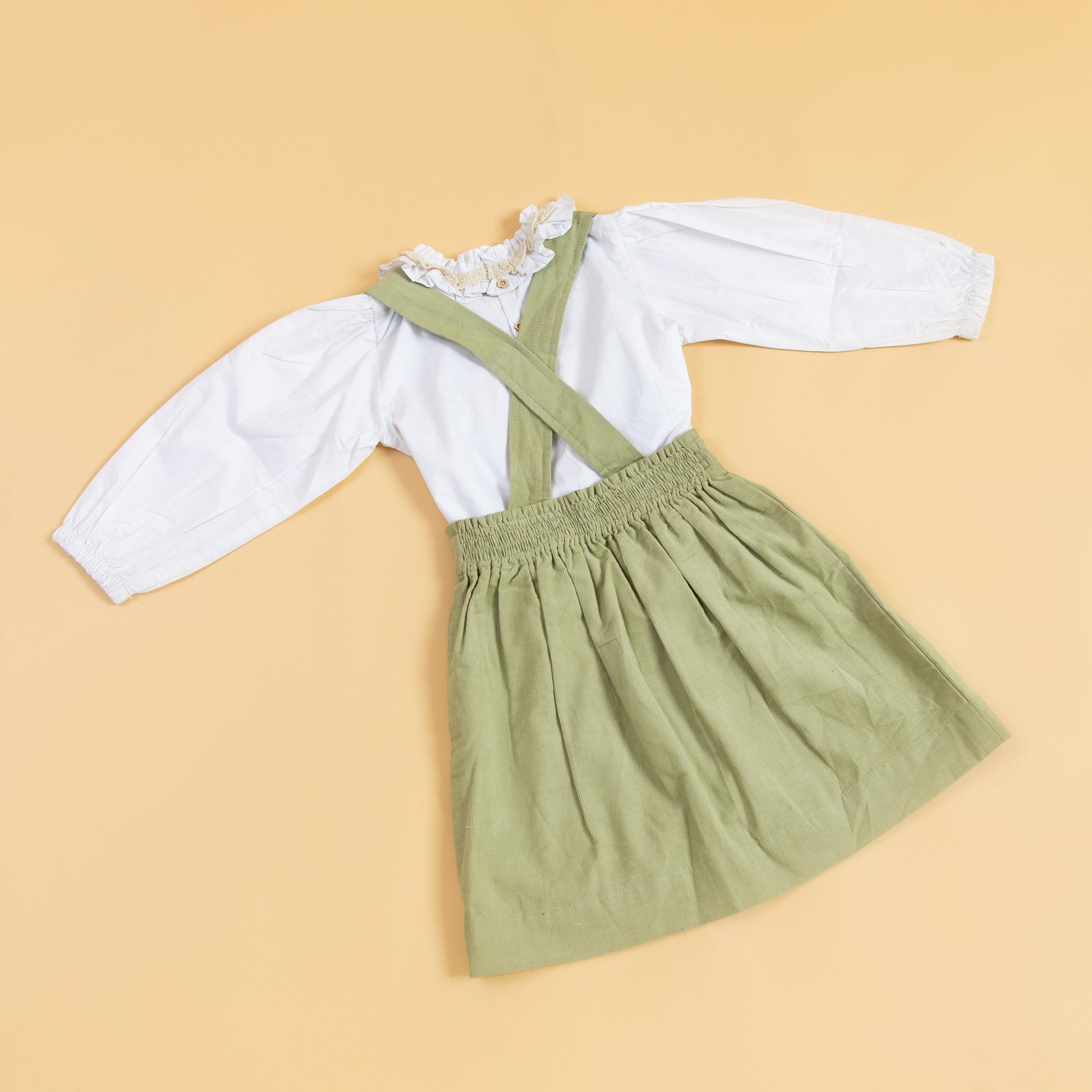Green children's pinafore dress with suspenders and a white ruffled shirt for playful outfits