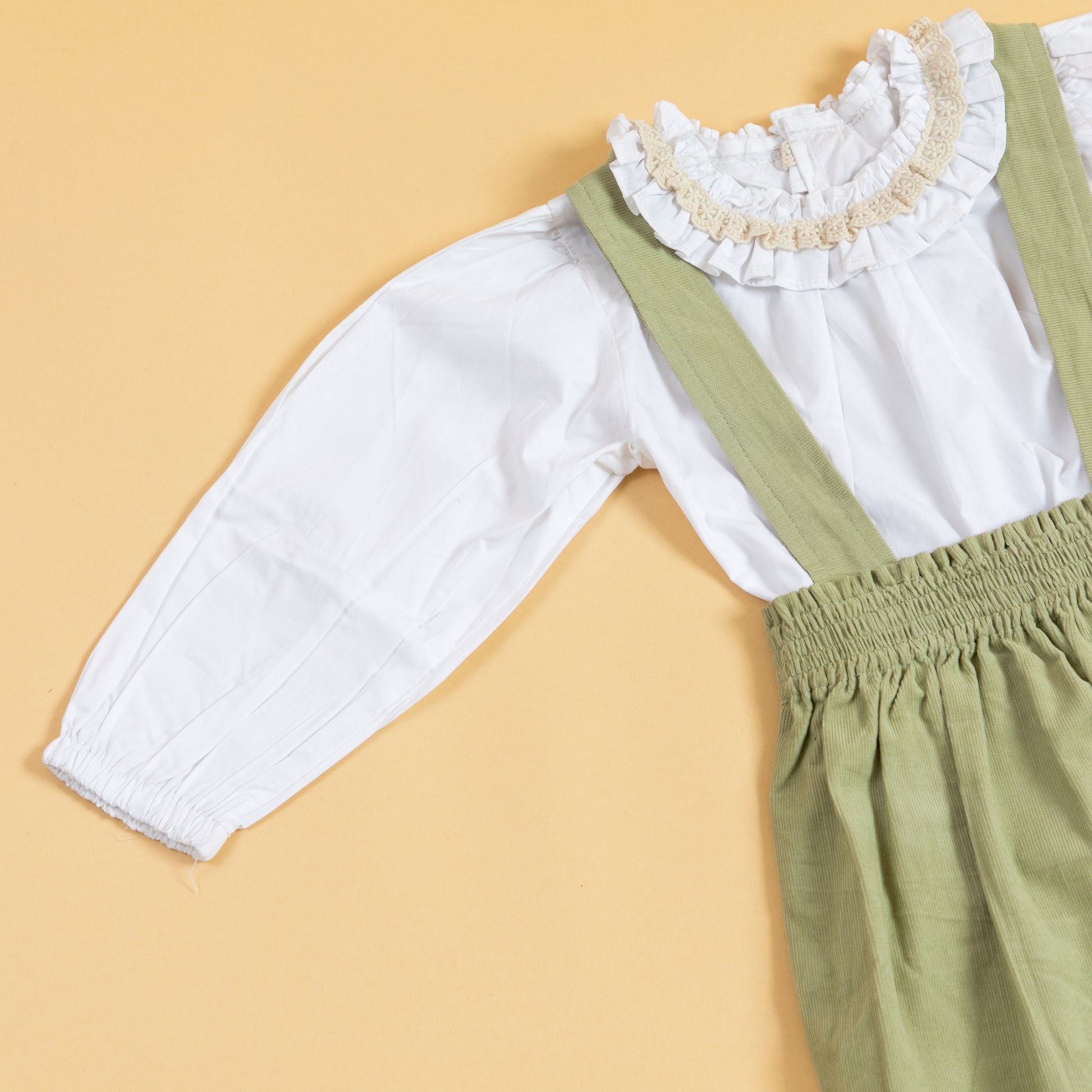 Children's pinafore dress with suspenders in green, paired with a white ruffled blouse for playful outfits