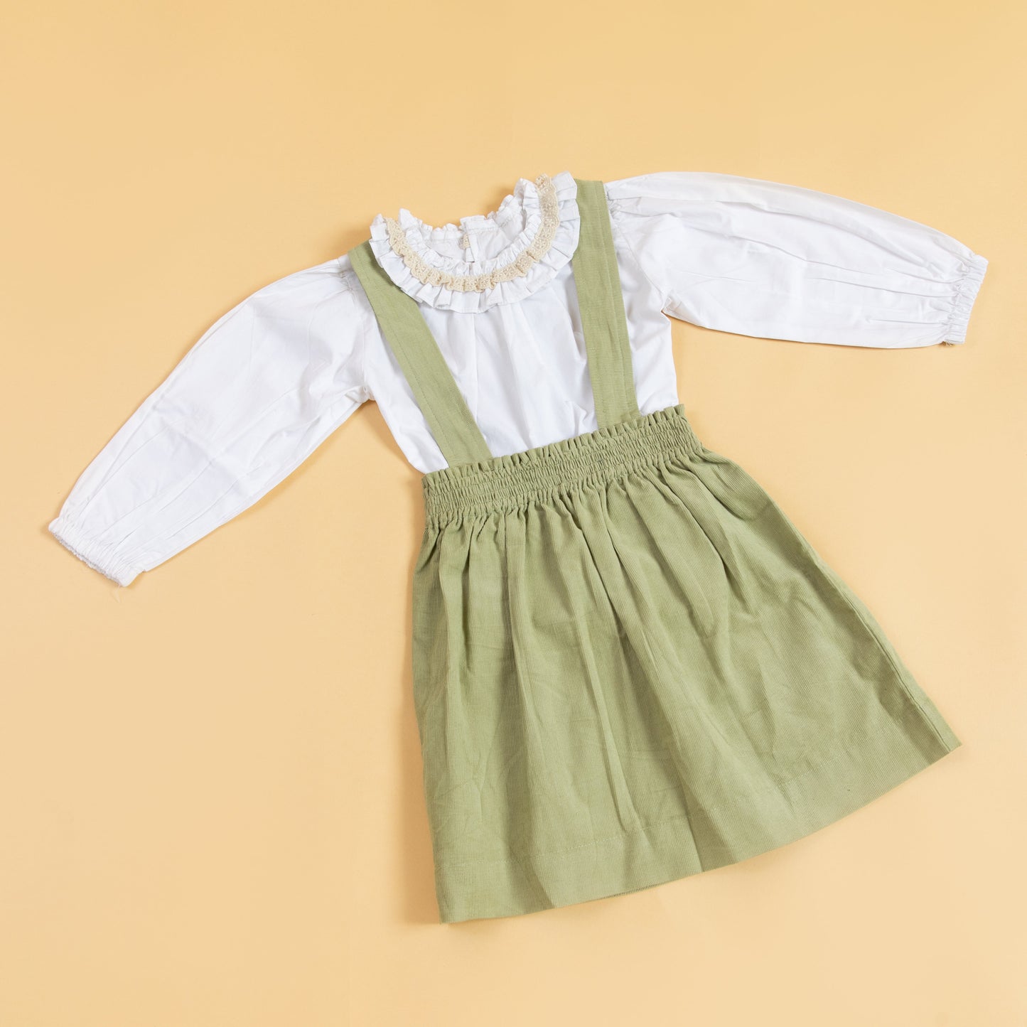 Children's pinafore dress with suspenders in light green paired with a white ruffled blouse