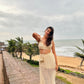 Woman in cream crochet two piece set on sea wall with palm trees and ocean breeze trendy seaside vacation outfit