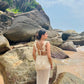 Woman wearing cream crochet open back dress on rocky beach showcasing Stylera trendy seaside vacation outfit