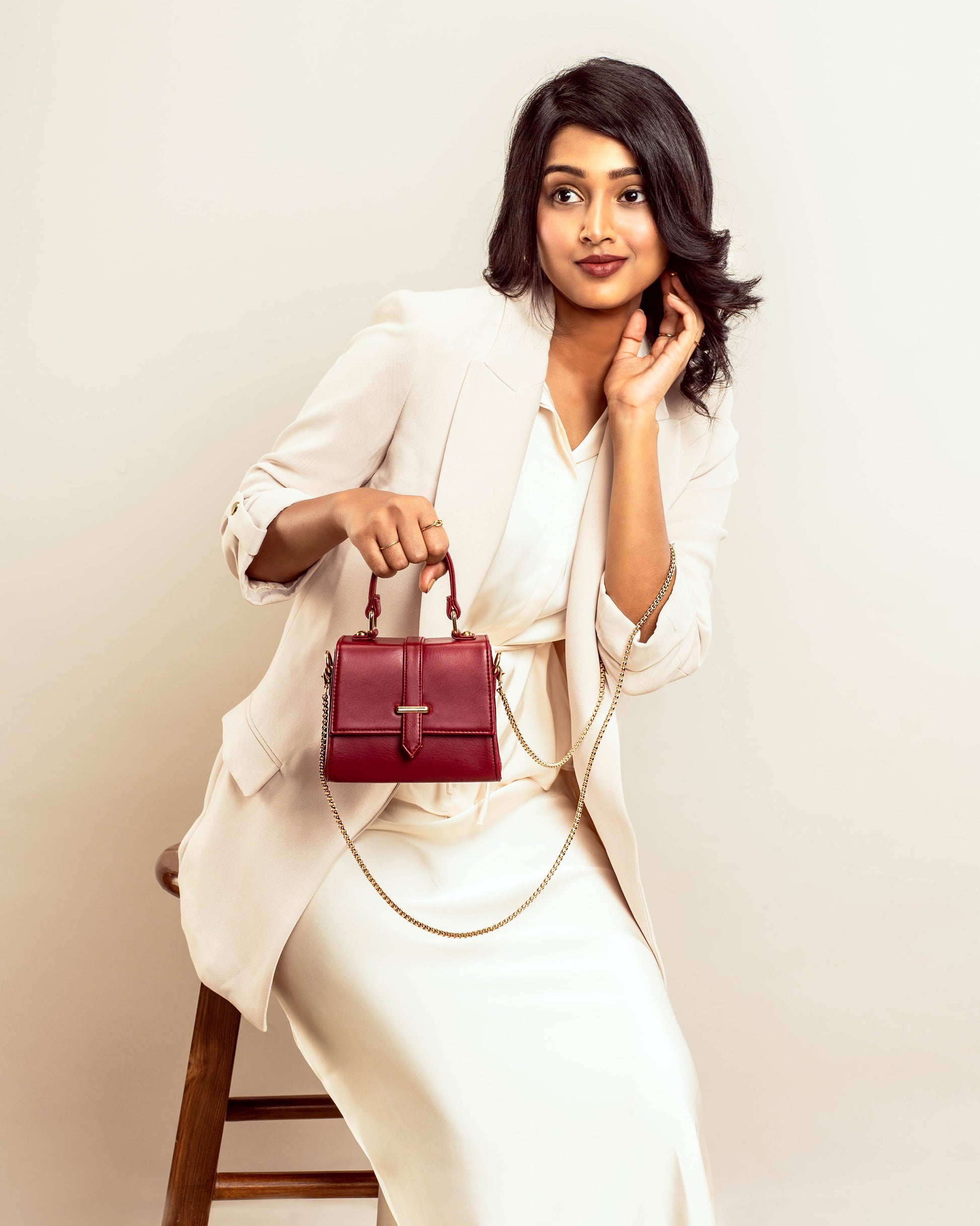 Stylish woman holding a crimson mini sling bag with a gold chain strap and elegant design