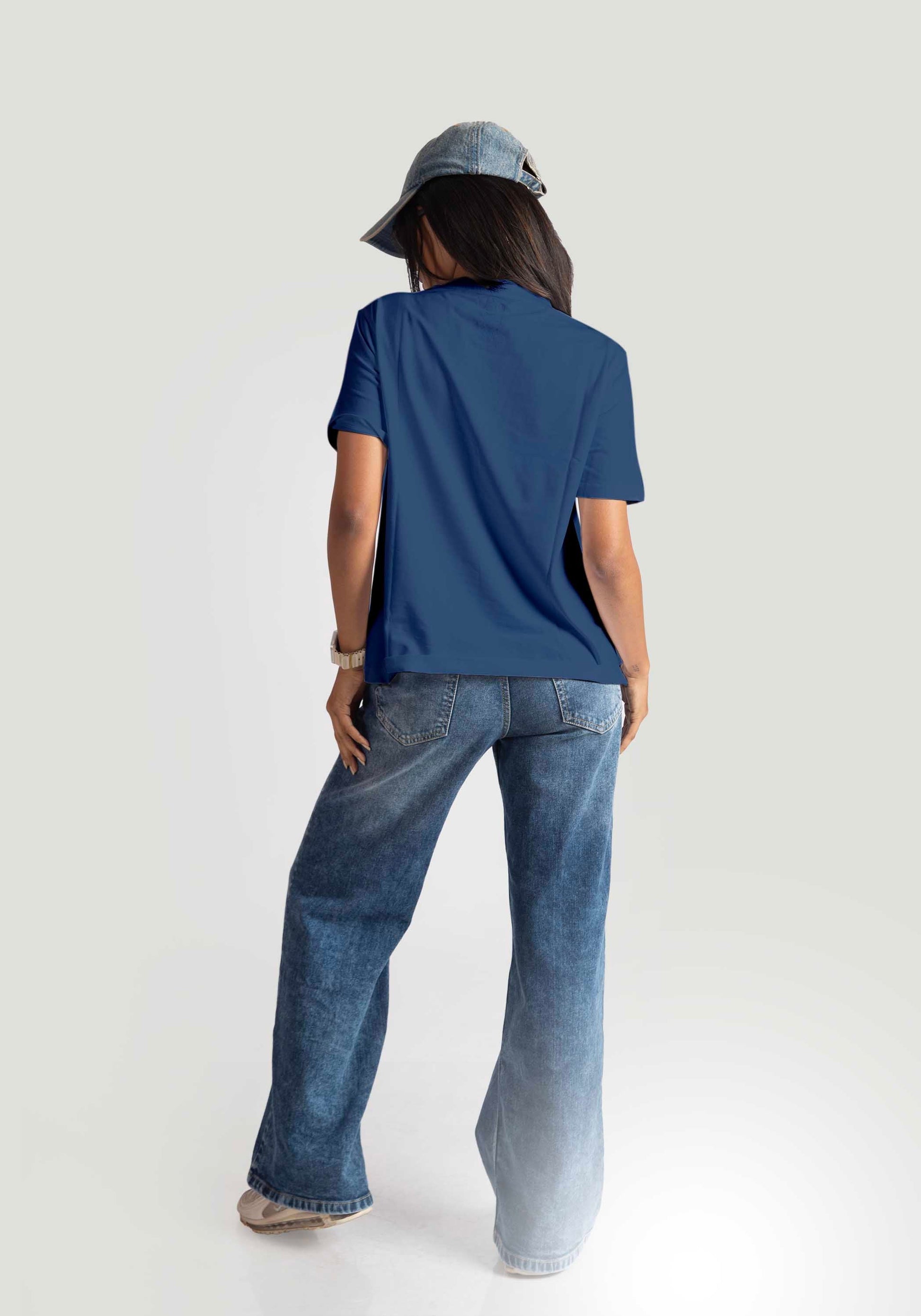 Back view of woman wearing cute print blue t-shirt for women paired with denim jeans and a cap