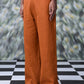 Dark camel linen trousers from Stylera worn with white sneakers on checkered floor