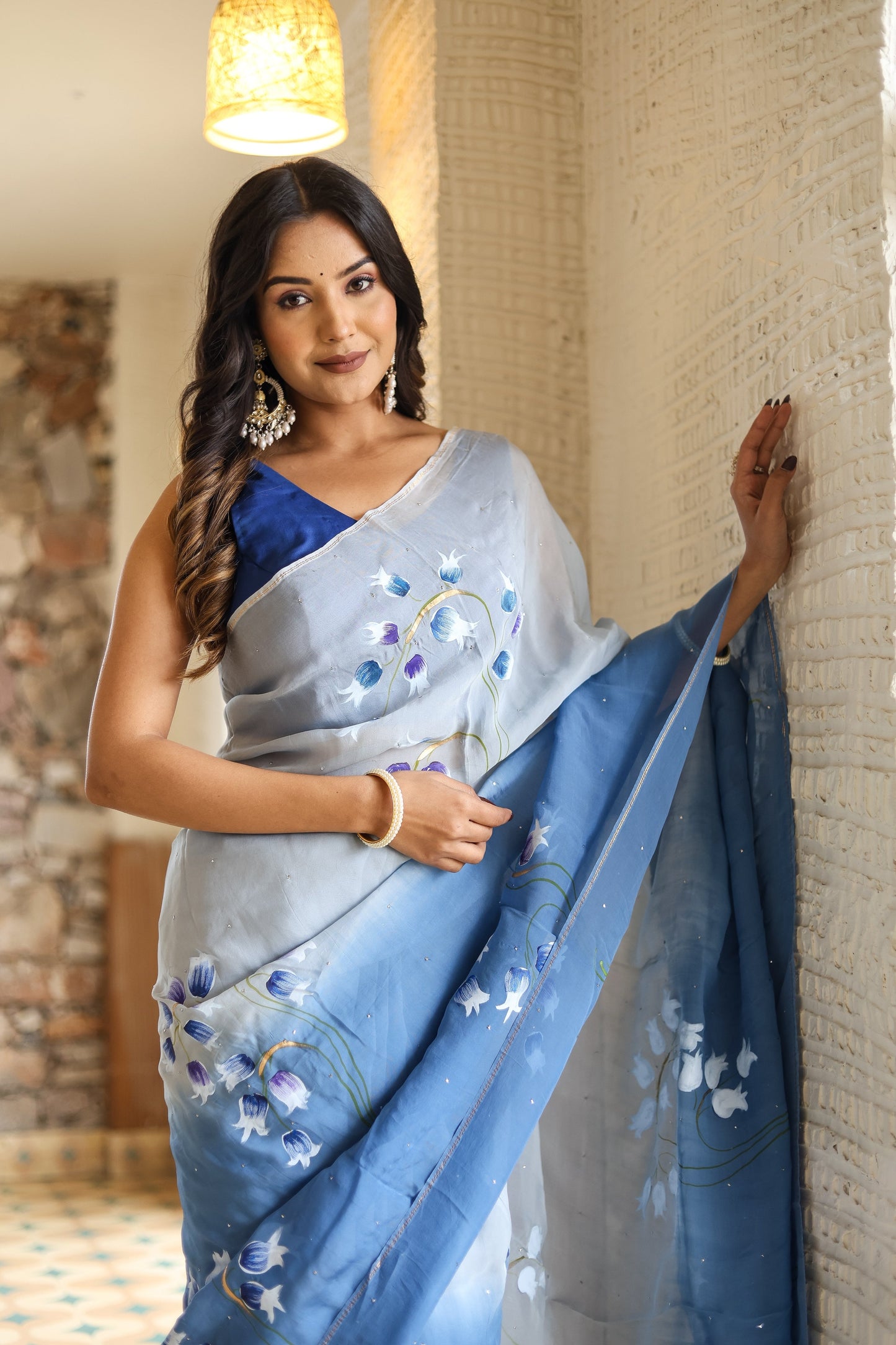 Elegant designer blue saree for women featuring floral patterns, styled with a blue blouse and hanging earrings