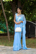 Elegant designer chiffon saree with floral painting in blue, styled with a white handbag and accessories