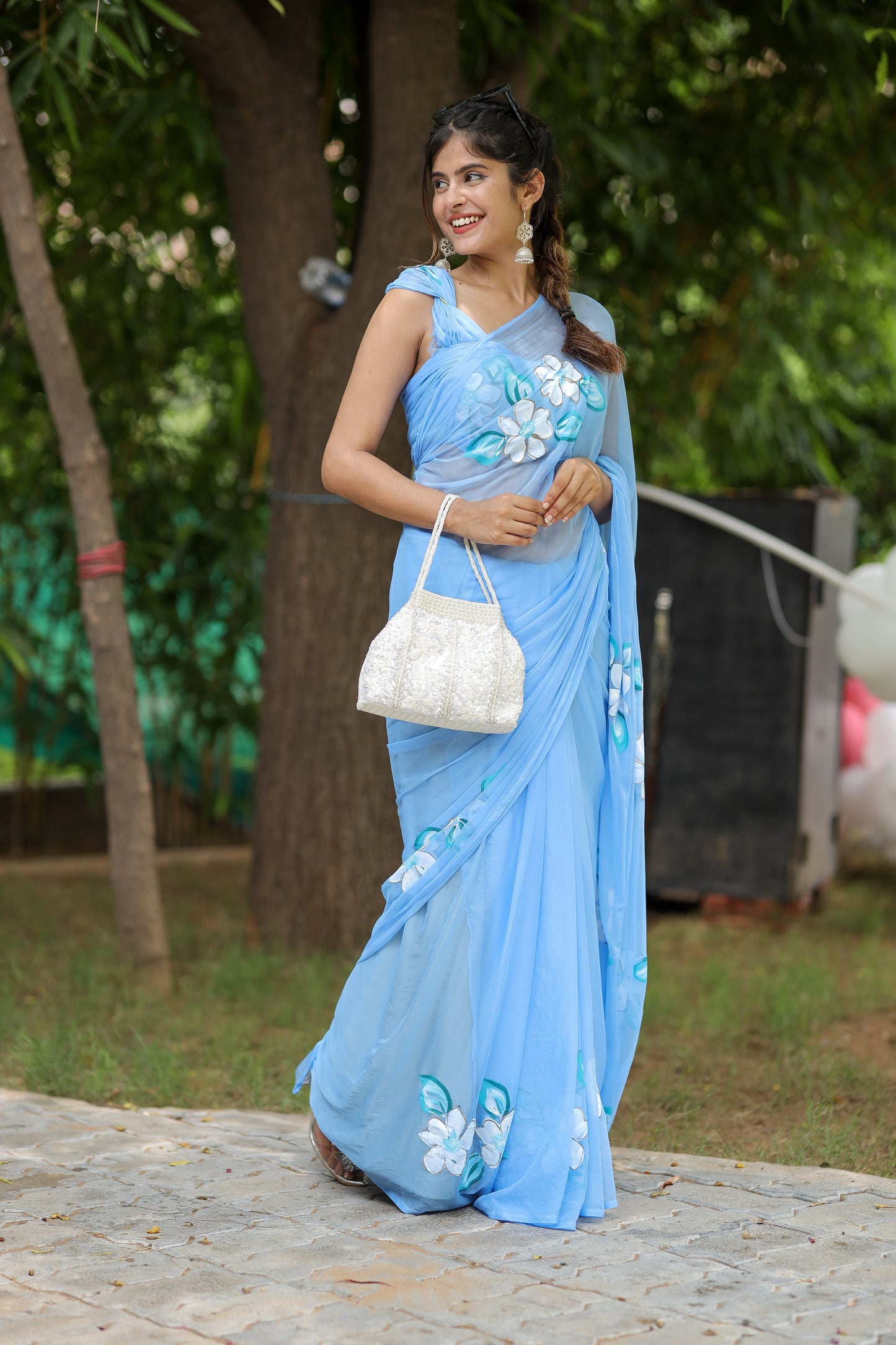 Elegant blue designer chiffon saree with floral painting draped beautifully on a model in a natural setting