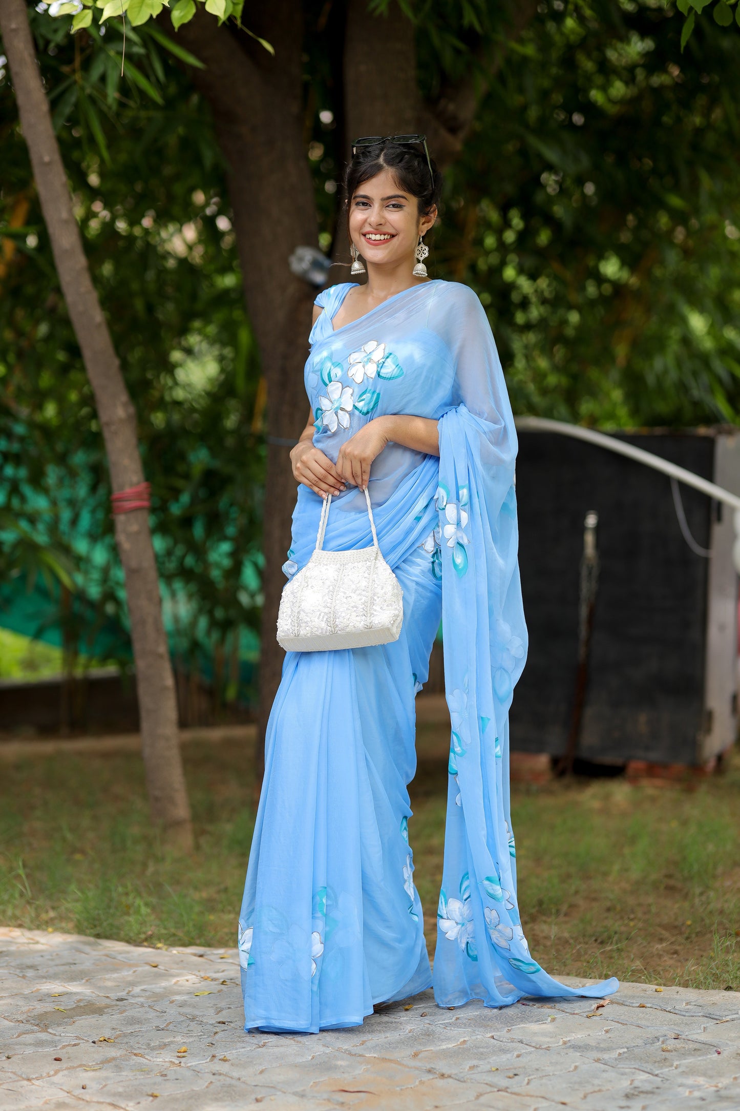 Elegant designer chiffon saree with floral painting in blue, worn by a model with stylish accessories