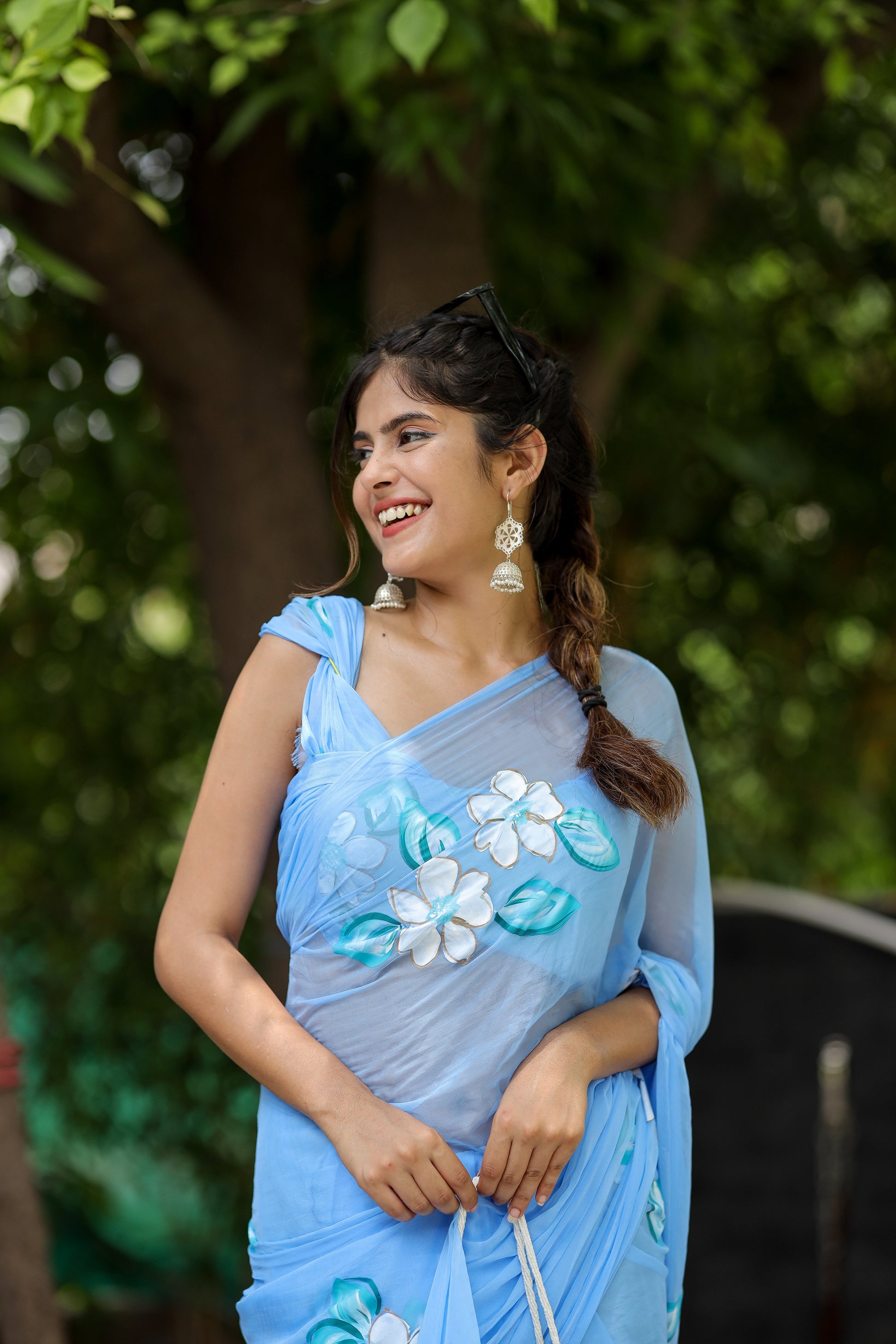 Model wearing a designer chiffon saree with floral painting in a serene outdoor setting