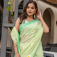 Elegant designer malmal saree with flowers in soft green color, worn by a woman with matching earrings