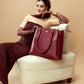 Stylera designer maroon handbag displayed on a stylish chair next to a model in elegant attire