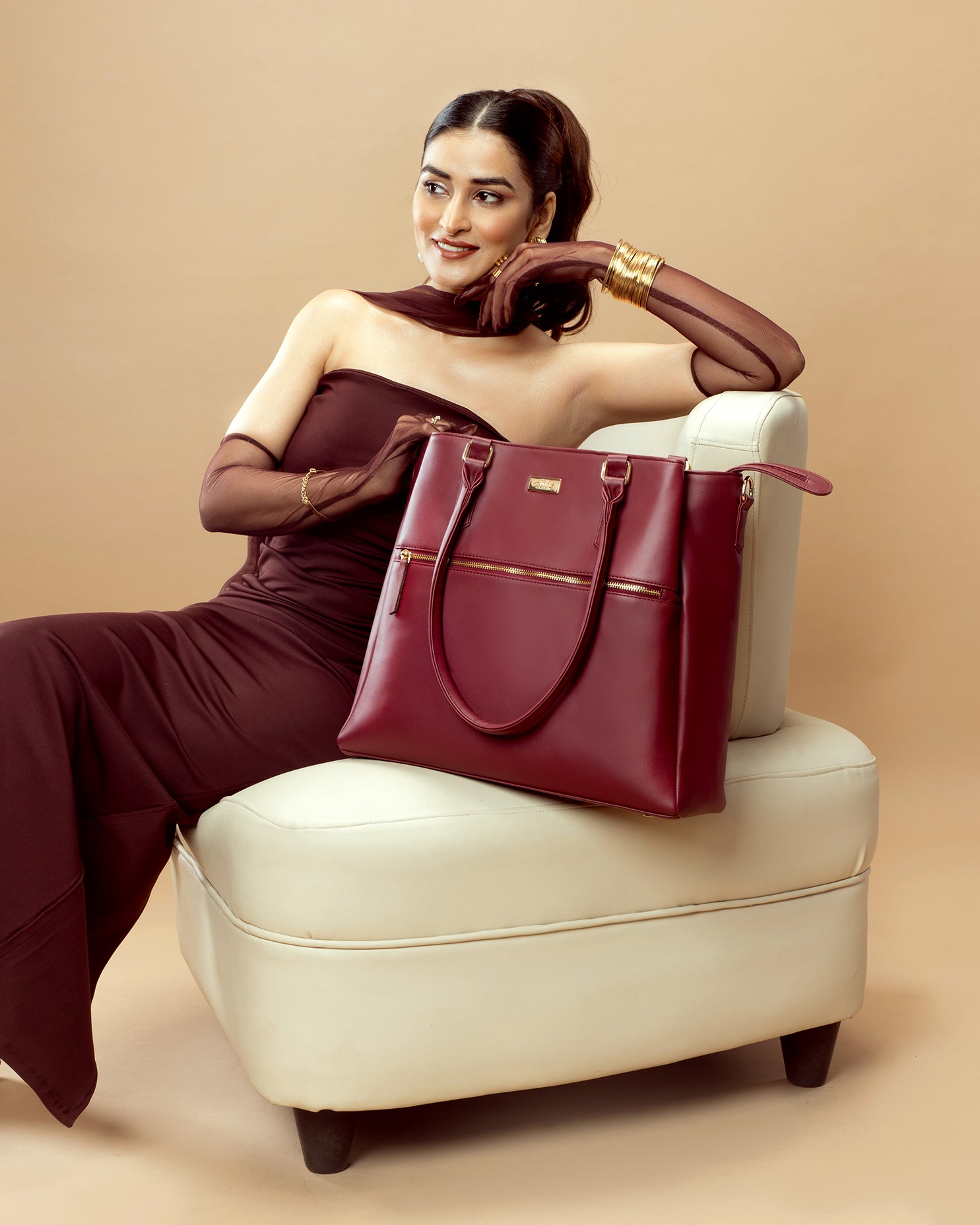 Stylera designer maroon handbag displayed on a stylish chair next to a model in elegant attire