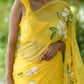 Bright yellow designer saree with floral art featuring elegant white blossoms and green leaves