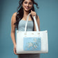 Model showcasing a large designer tote bag with floral painting on a blue background