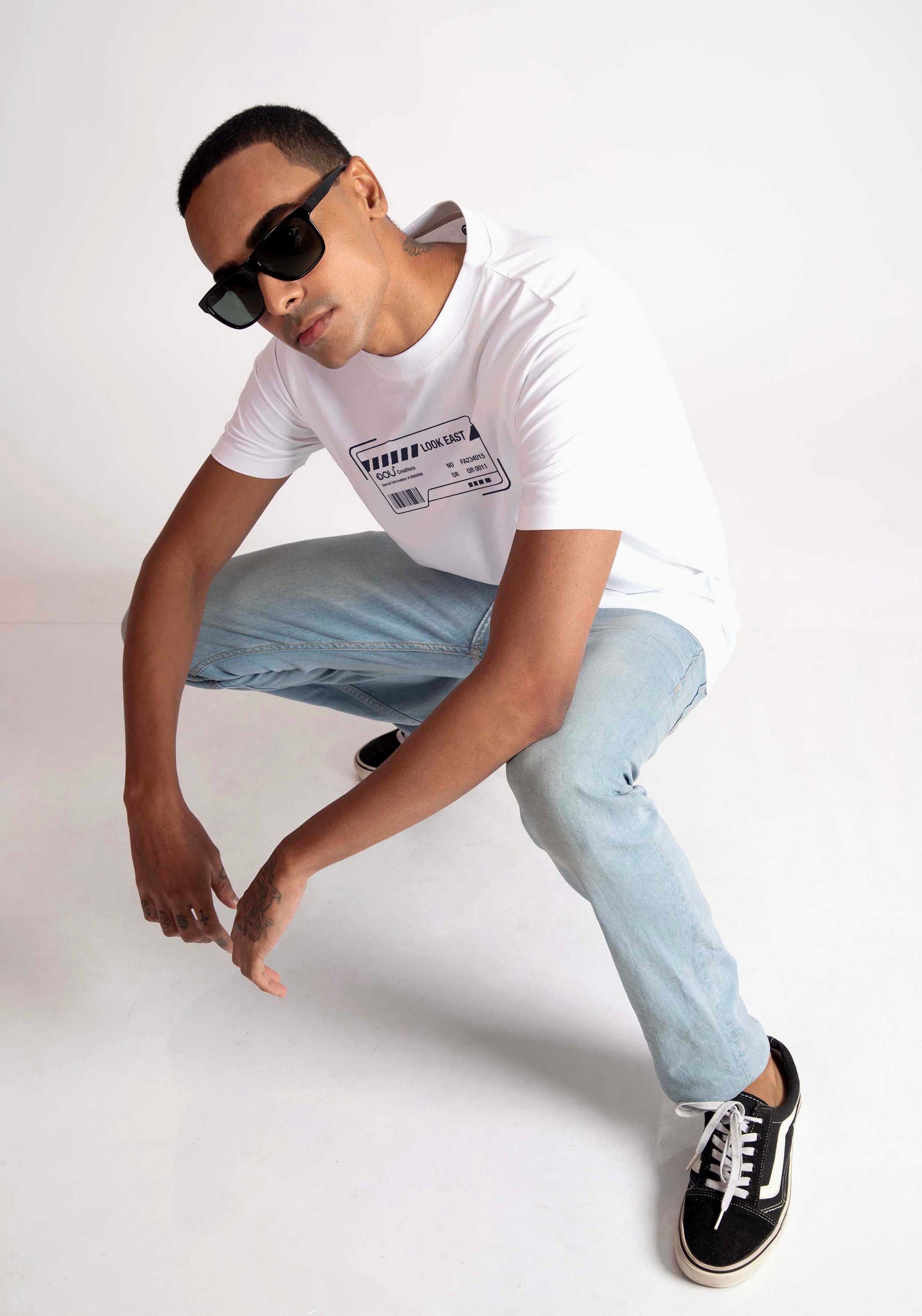 Man wearing Stylera white regular fit t-shirt with graphic print paired with light blue jeans and black sneakers