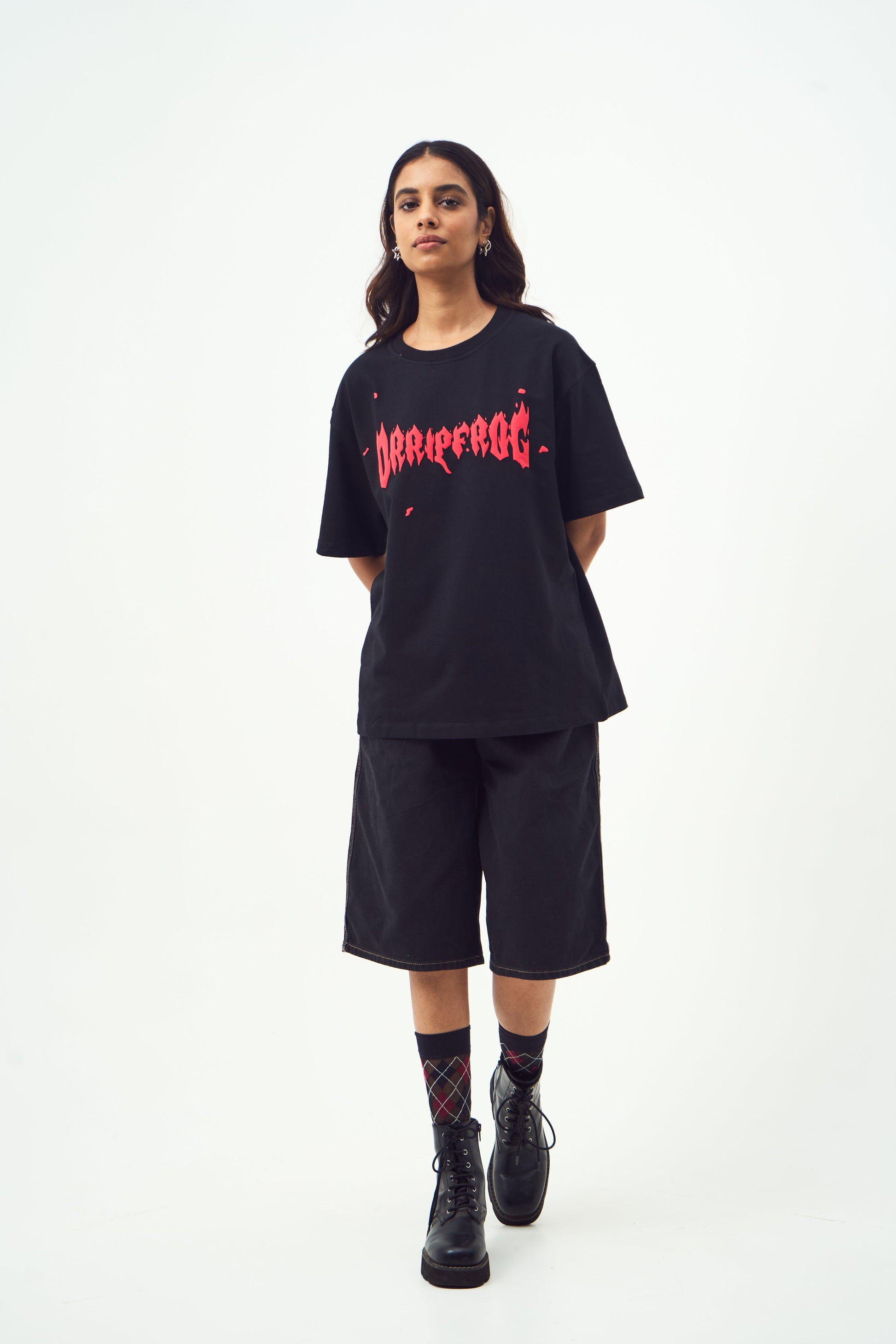 Model wearing Stylera black oversized edgy graphic tee for men and women with long shorts and combat boots