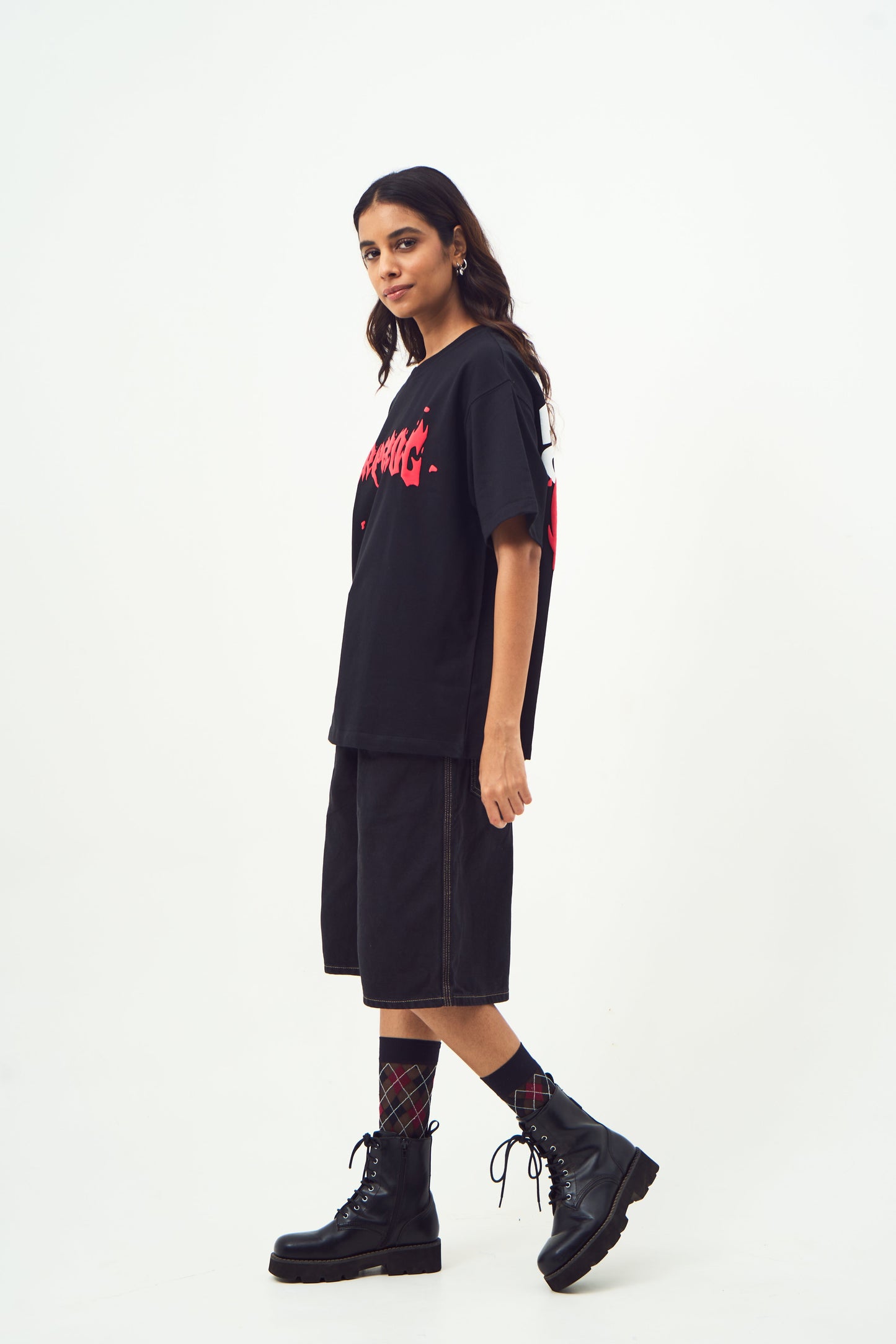 Model wearing Stylera black oversized edgy graphic tee for men and women with knee length shorts and combat boots