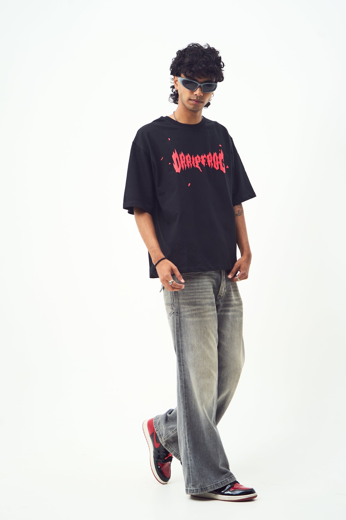 Model in black oversized edgy graphic tee for men and women paired with faded jeans red black sneakers