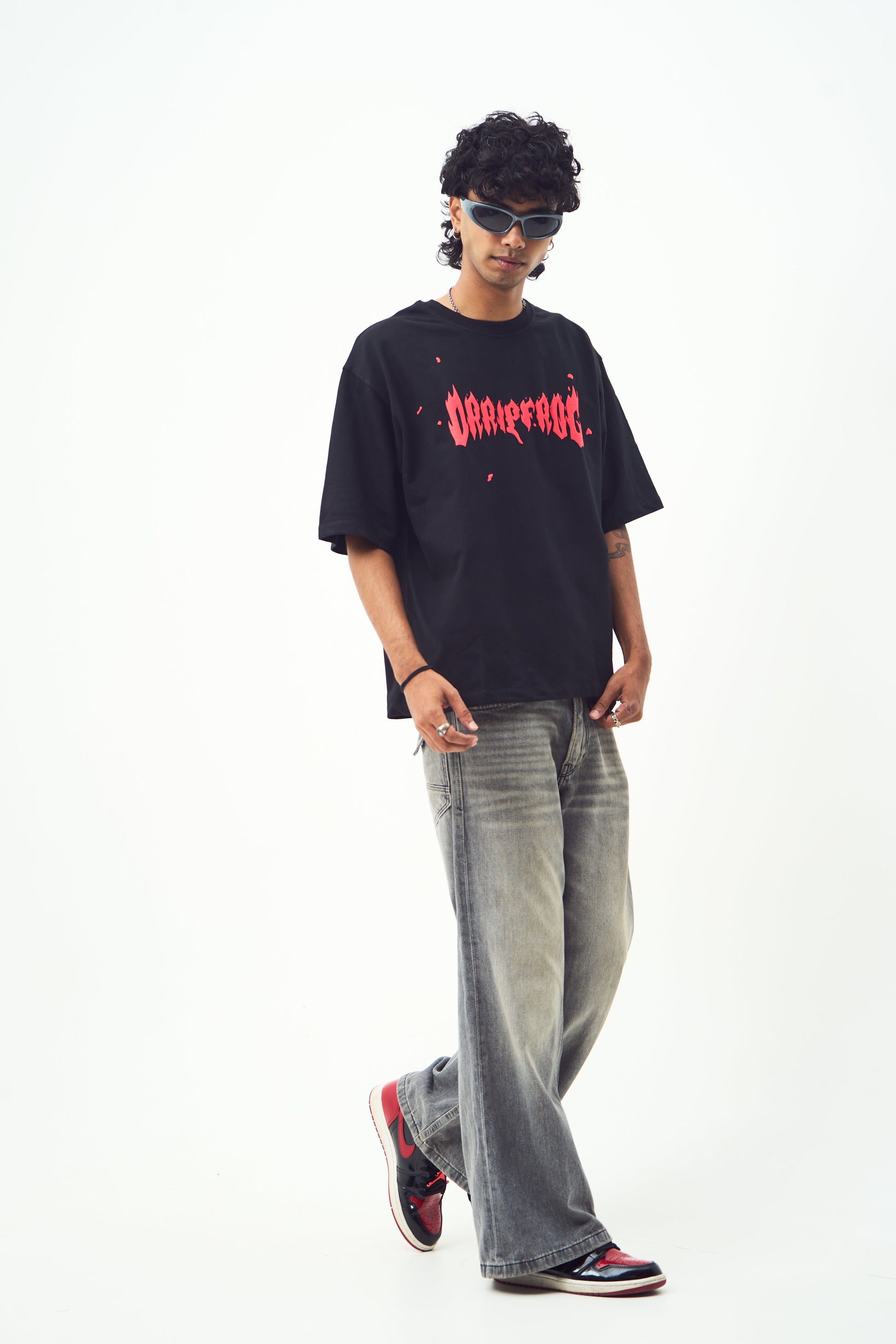 Model in black oversized edgy graphic tee for men and women paired with faded jeans red black sneakers