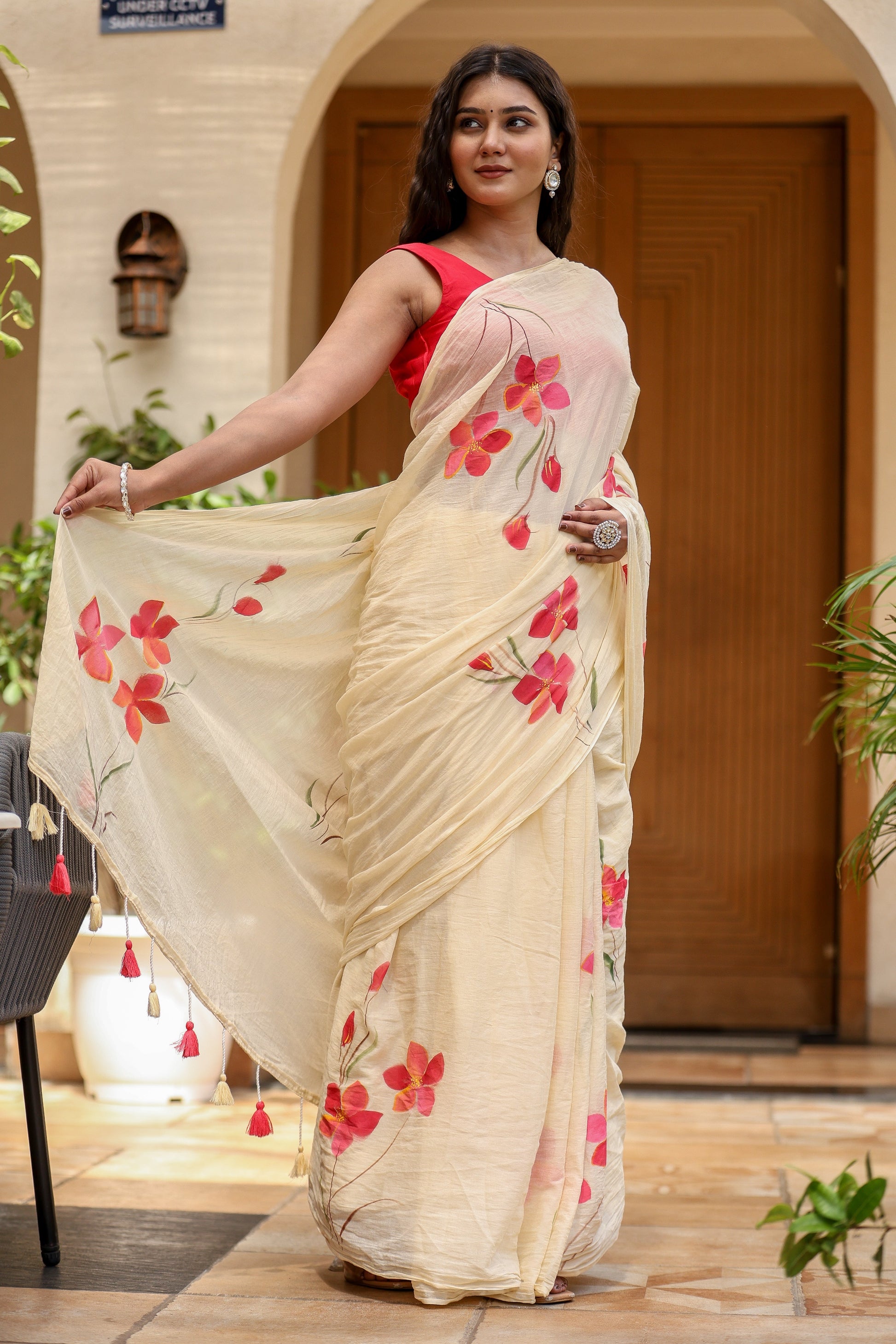 Elegant floral print cream saree with red flowers and delicate tassels for festive occasions